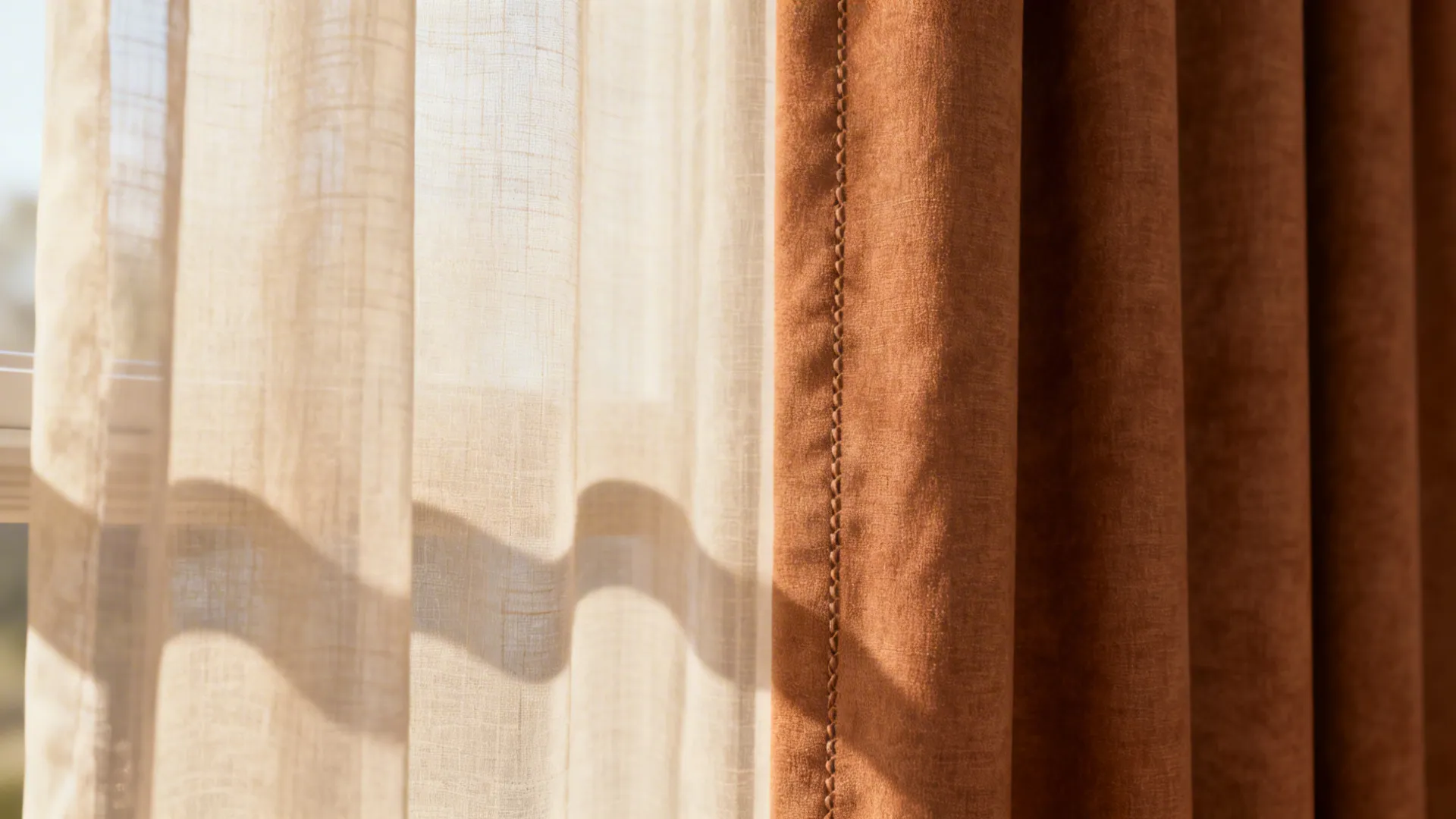 Close-up of light beige sheer layered over warm brown drape showing fabric texture and soft daylight