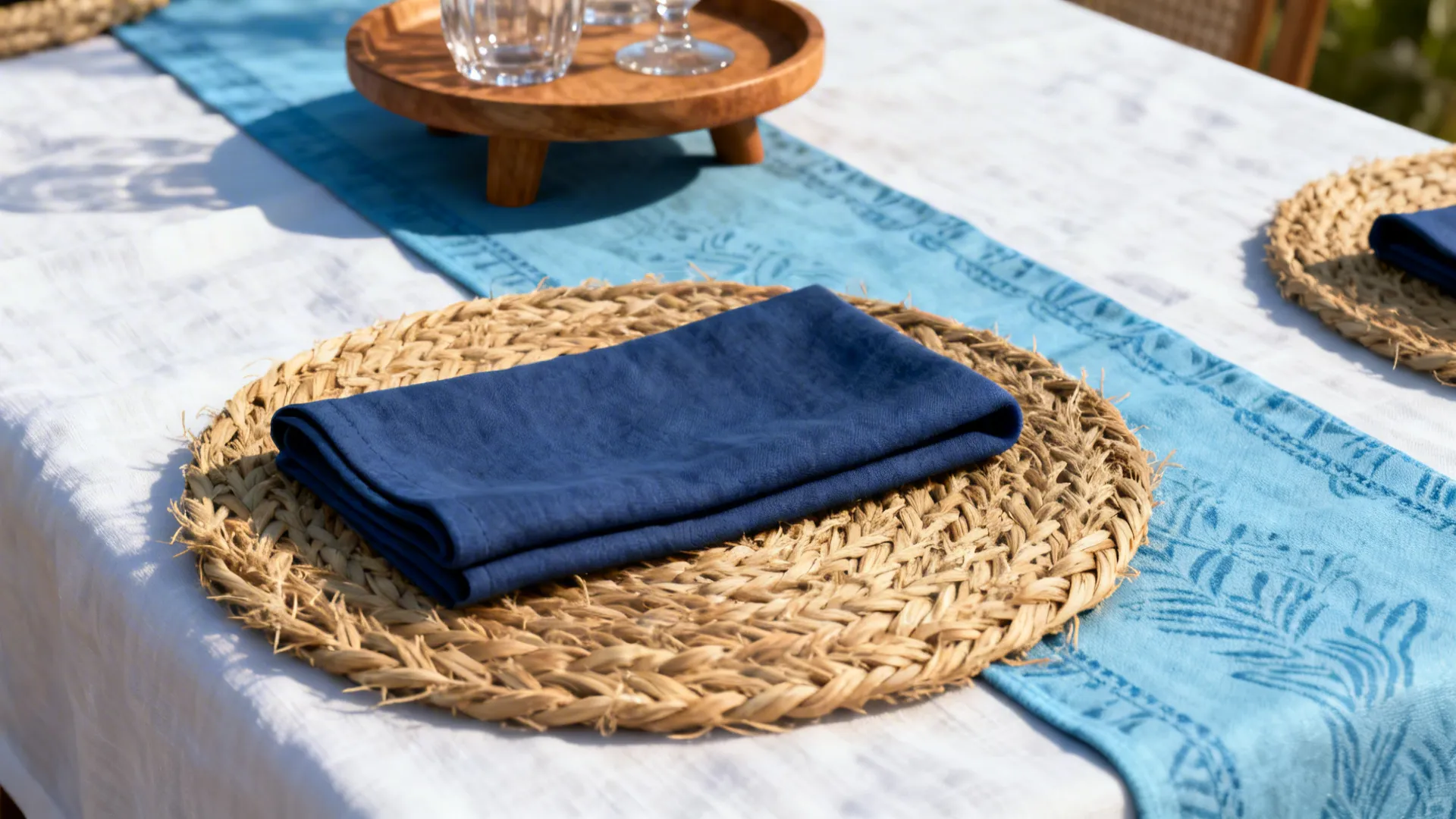 Close-up of layered white linen, indigo napkin and seagrass charger on a small table
