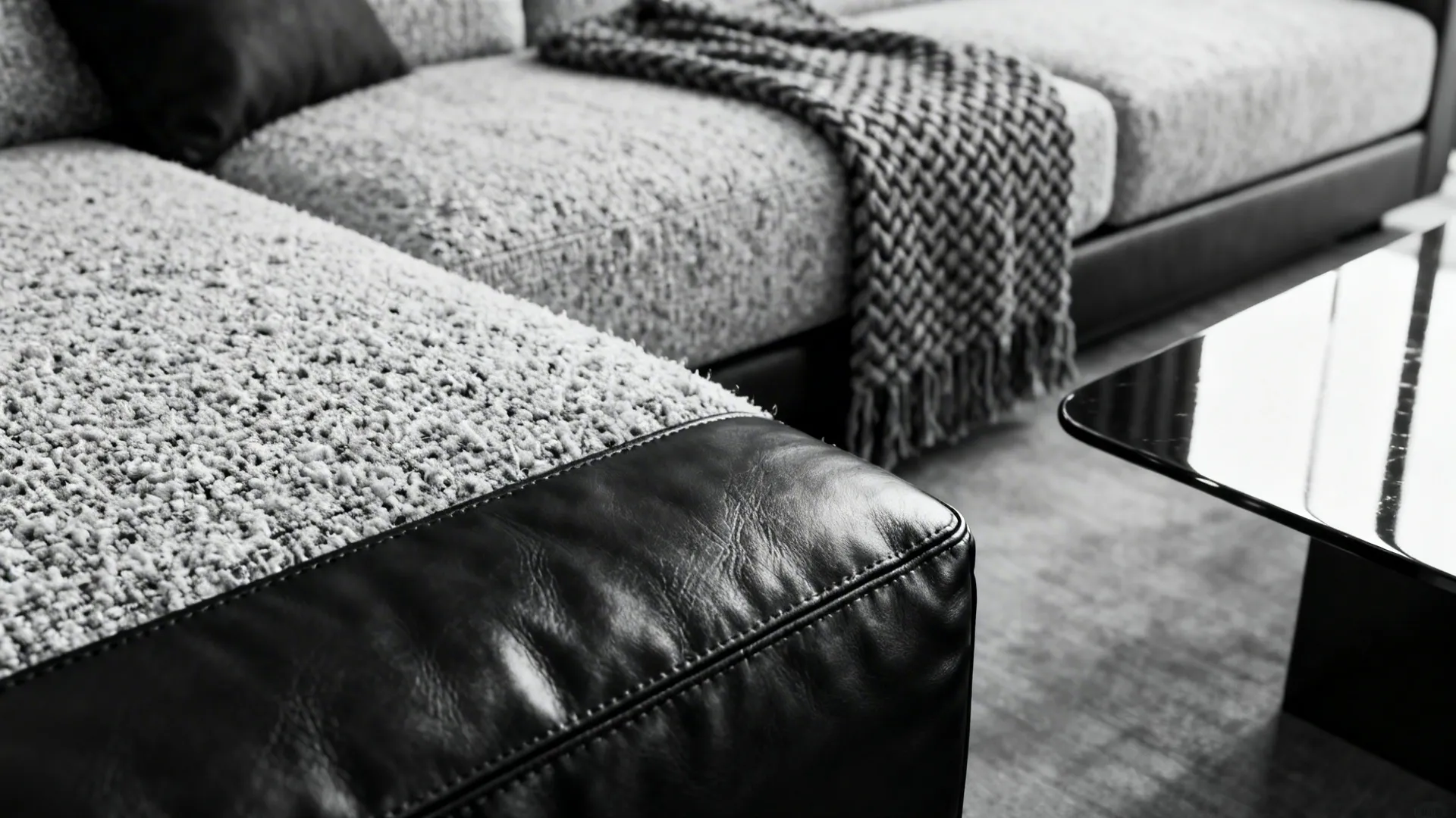 Macro view of boucle fabric, leather, woven throw and glossy table in monochrome tones.
