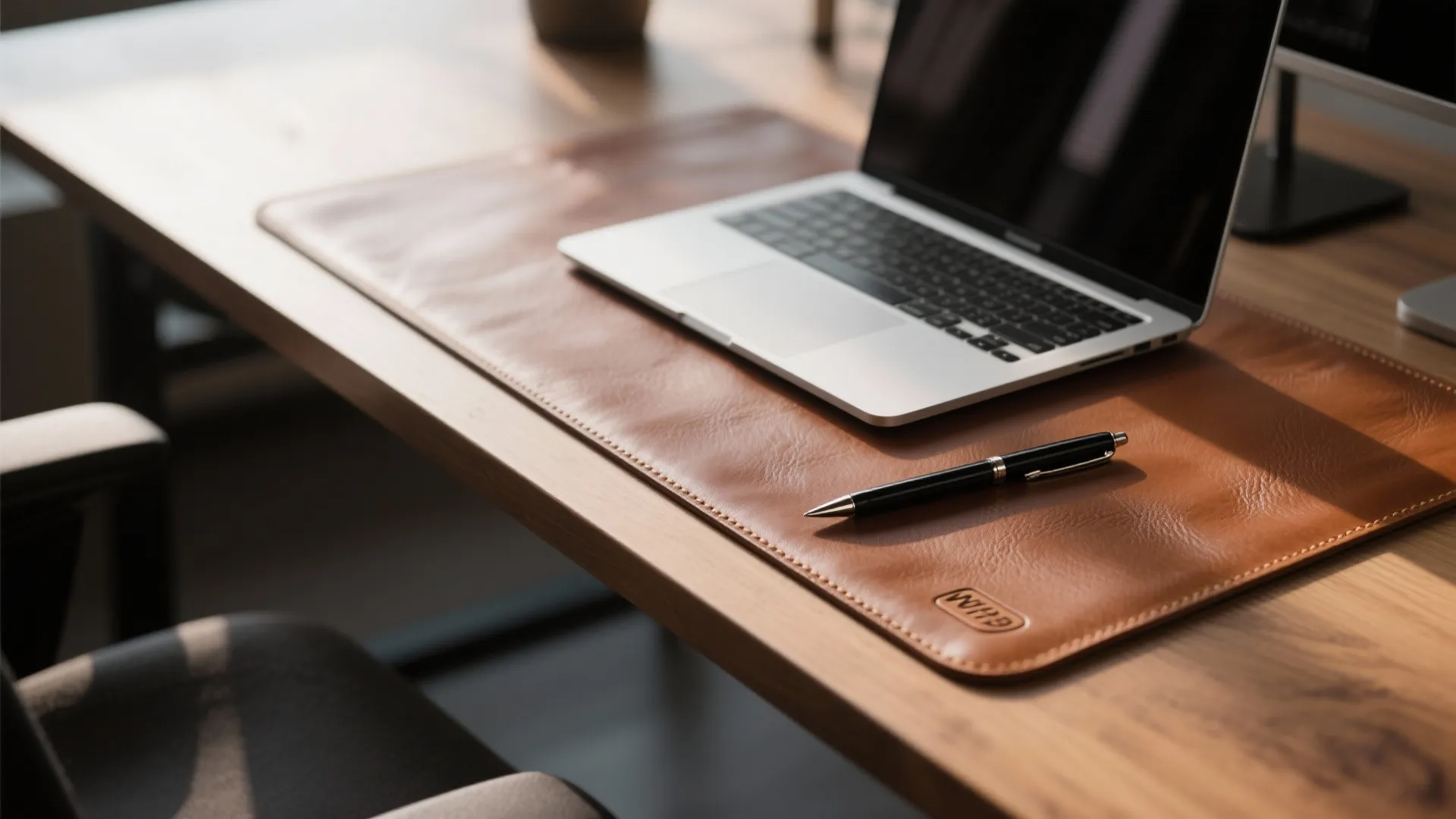 Brown leather desk mat on wooden table with laptop and black pen in natural light