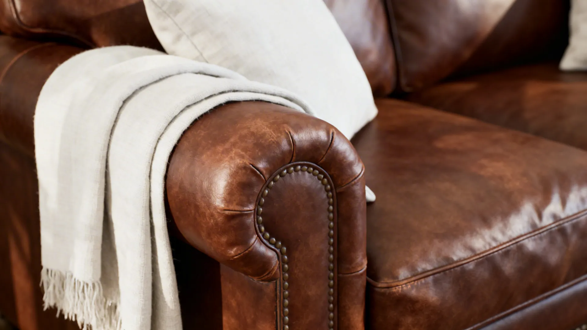 Detail of brown leather sofa with white linen throws and cushions, showing texture and removable covers