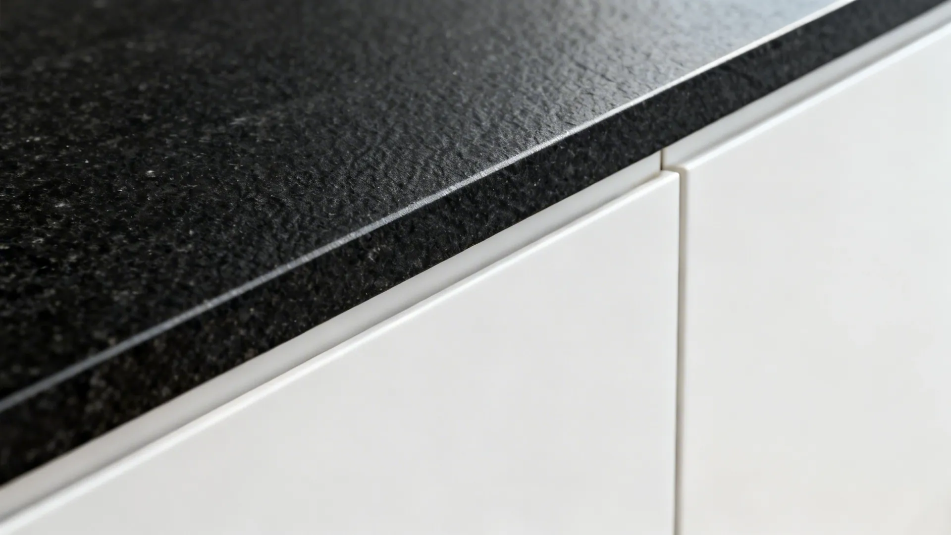 Macro of leathered black granite edge against a matte white cabinet front.