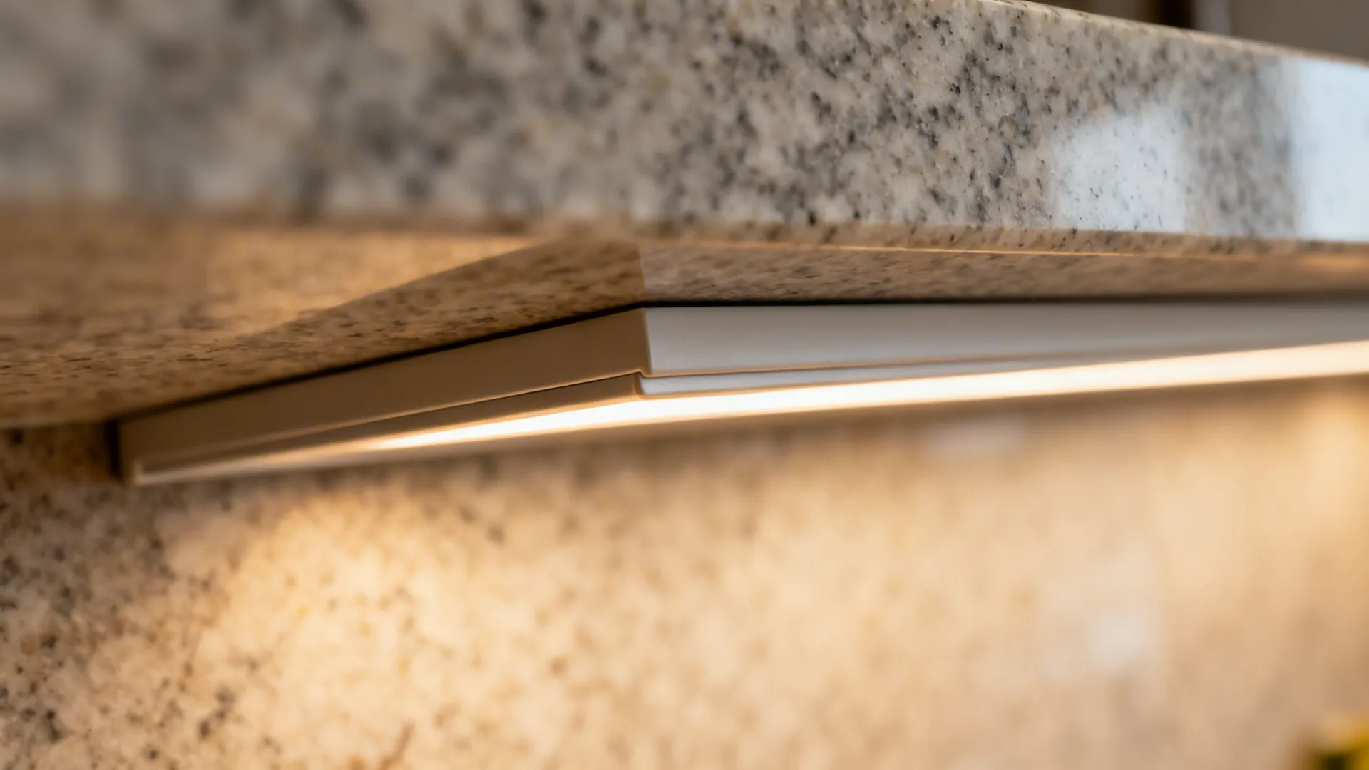 Macro view of a recessed LED channel beneath a honed granite shelf with a subtle concealing lip.