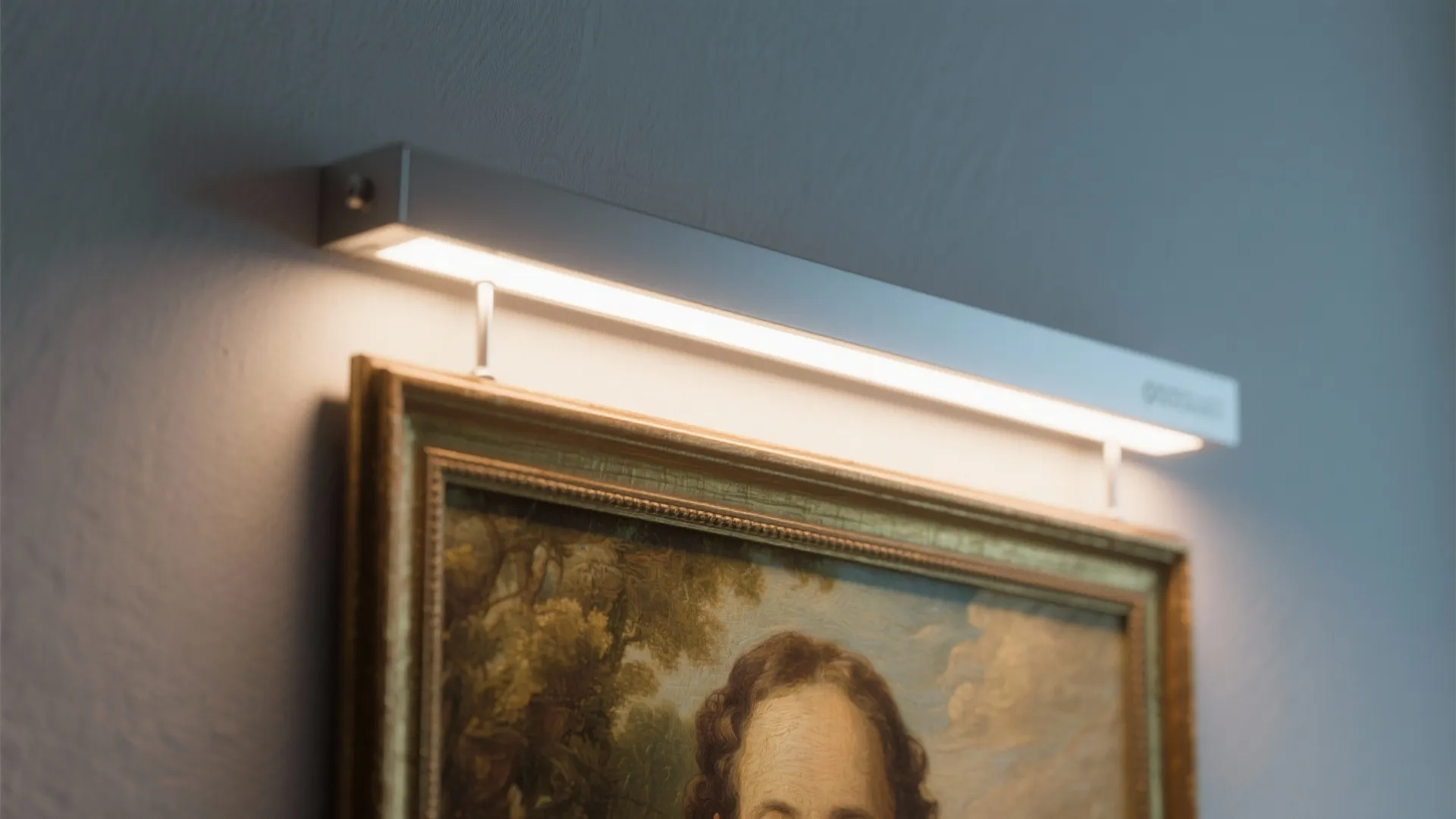 Modern silver led light fixture shining down on a classic framed painting on a grey wall