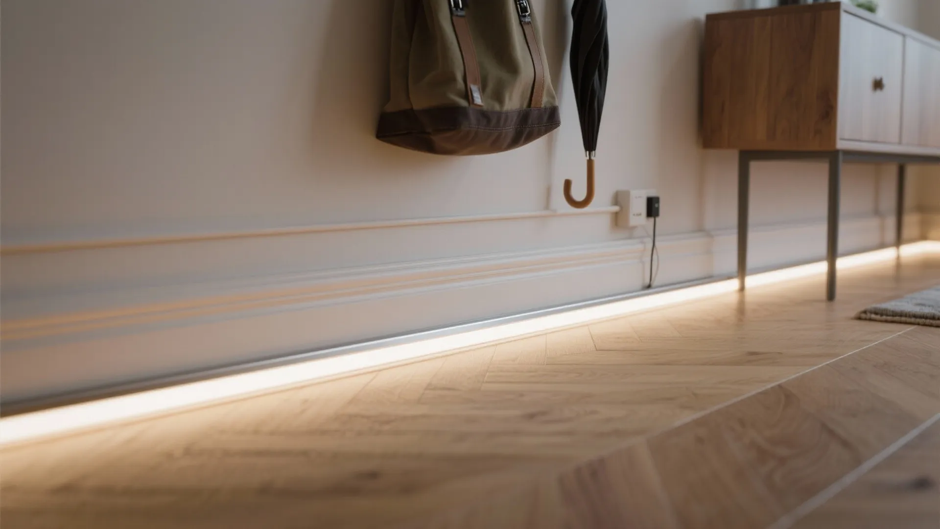 Modern white wall panel with floor light strip illuminating a light brown wood floor hallway