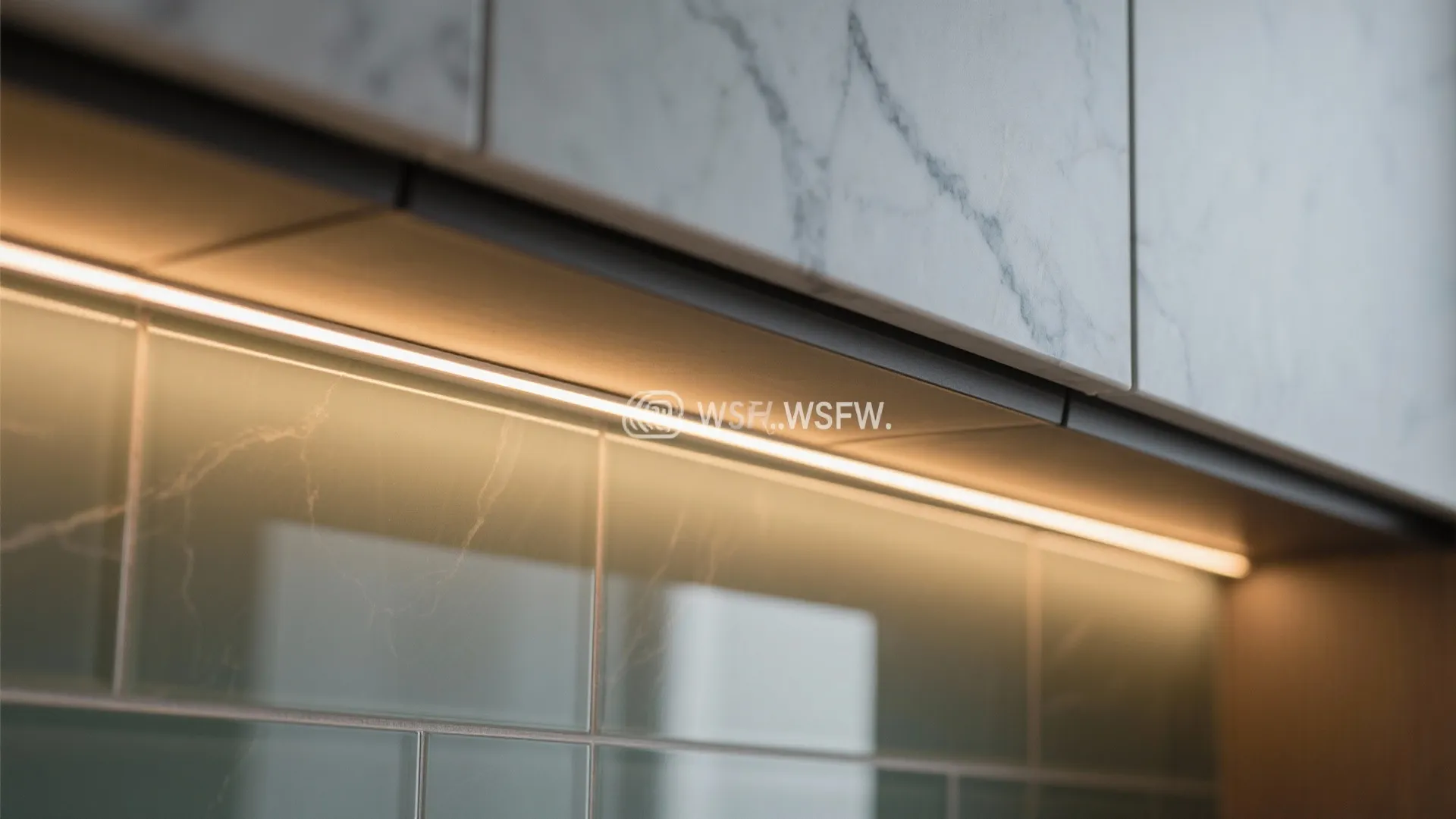 Macro of warm LED strip under cabinet illuminating a glass backsplash and quartz edge.