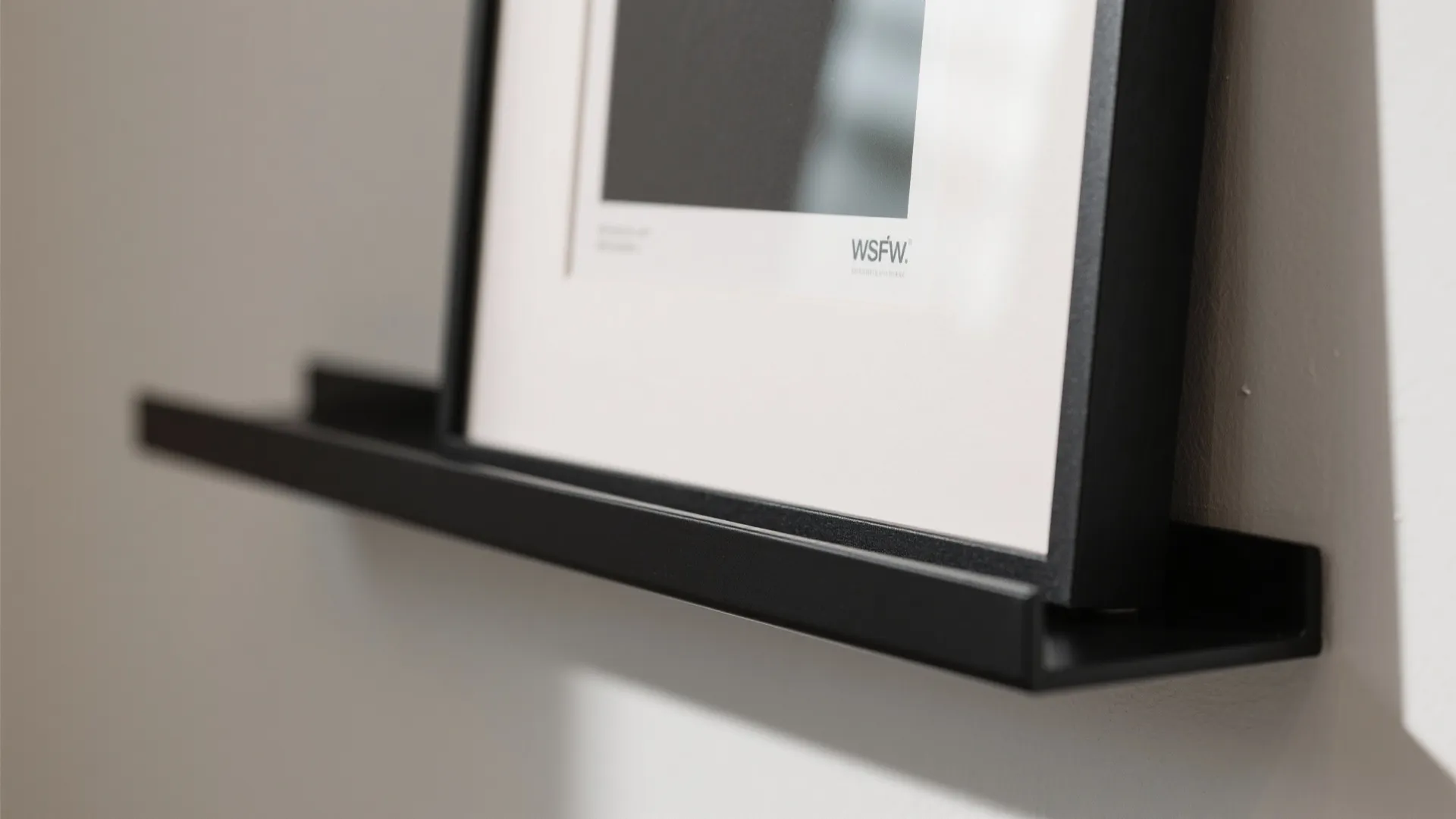 Black metal shelf holding a framed picture on a white wall with soft natural light