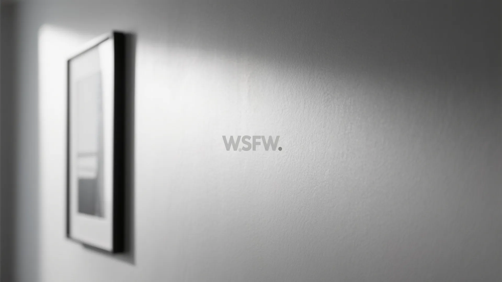 Close up view showing light reflecting on grey wall next to a black framed picture