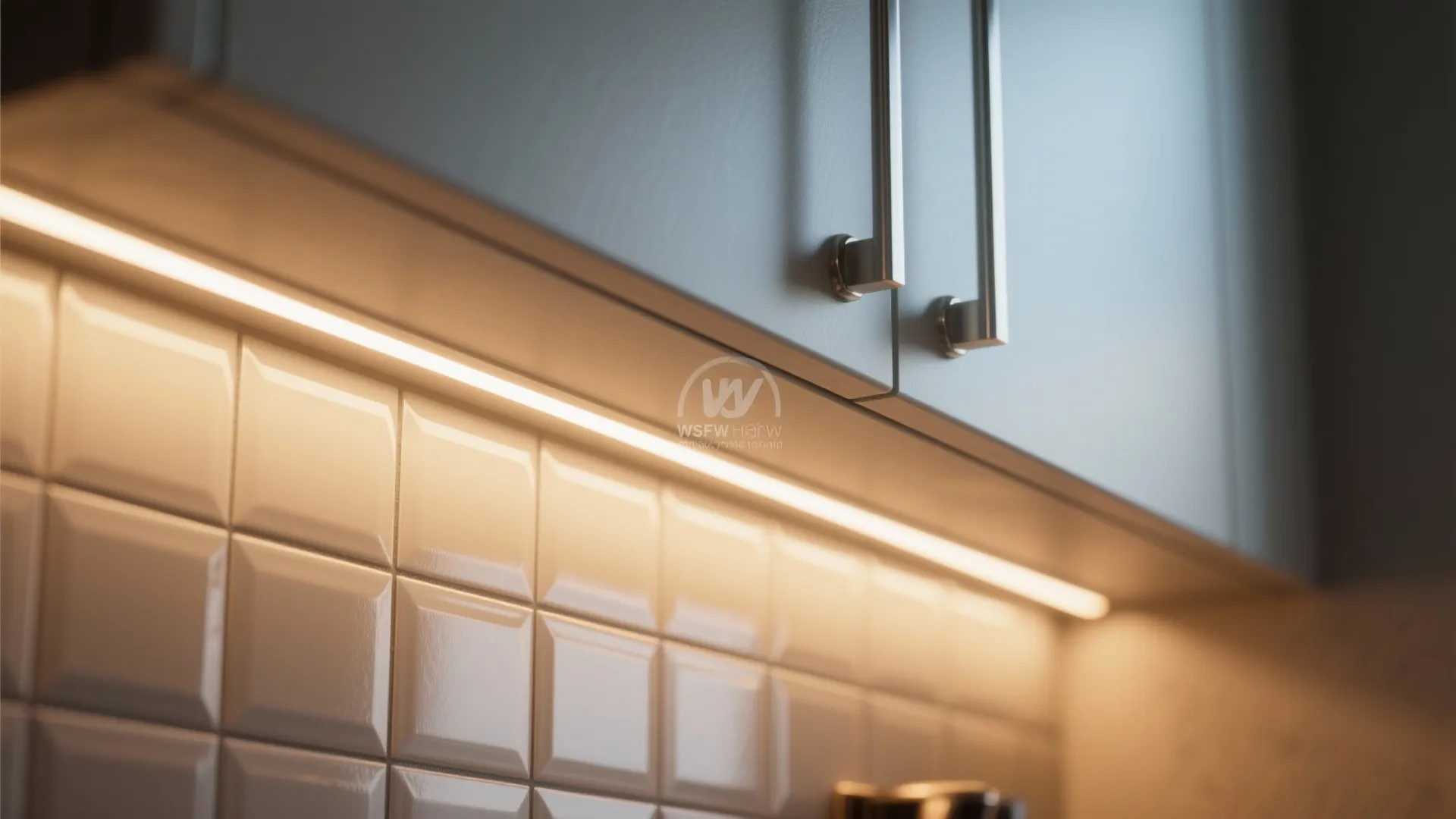 Close up of warm light fixture strip under kitchen cabinet with white square wall panel tiles