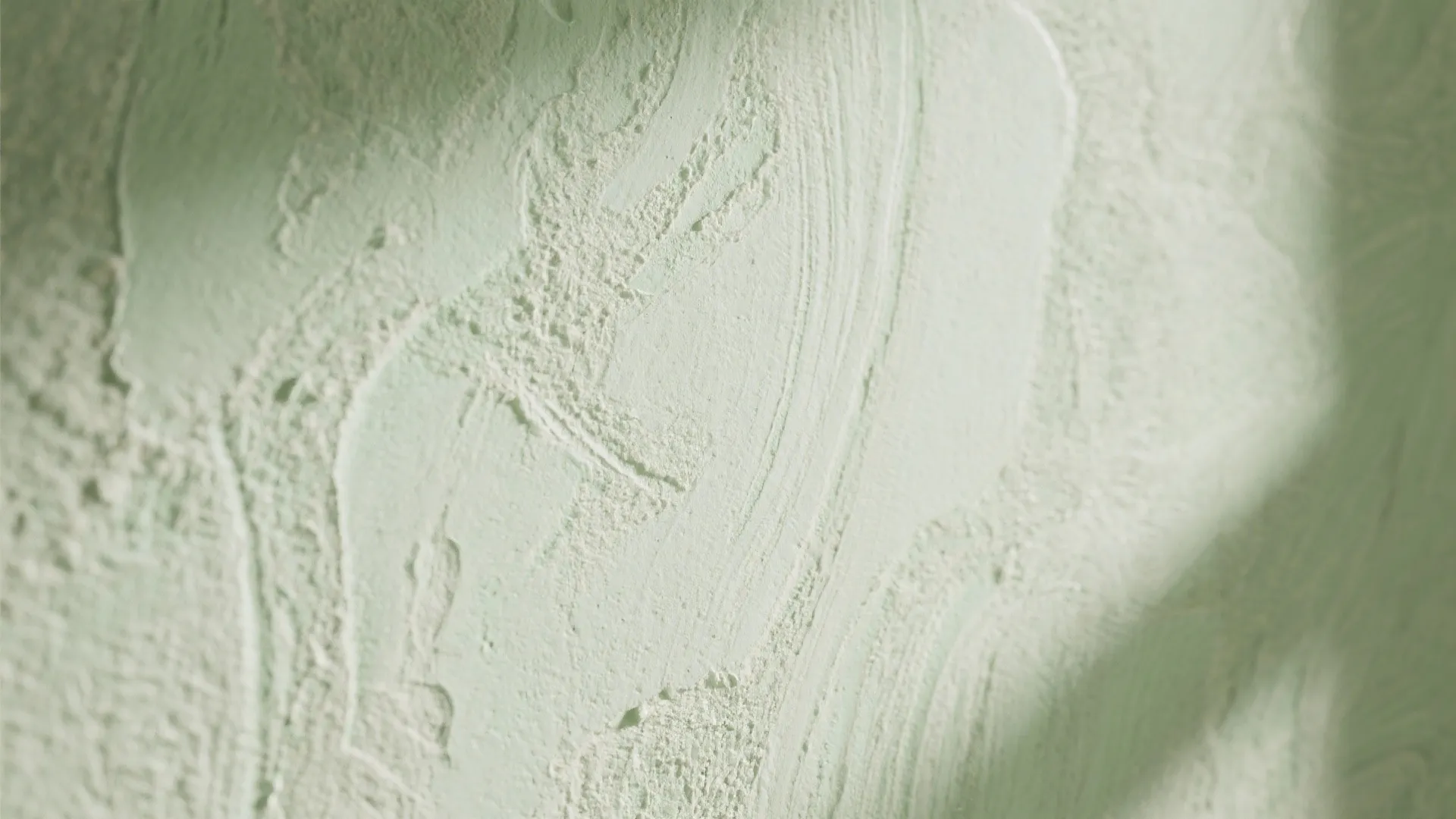 Close up of light green wall panel with rough plaster texture and soft shadows on surface