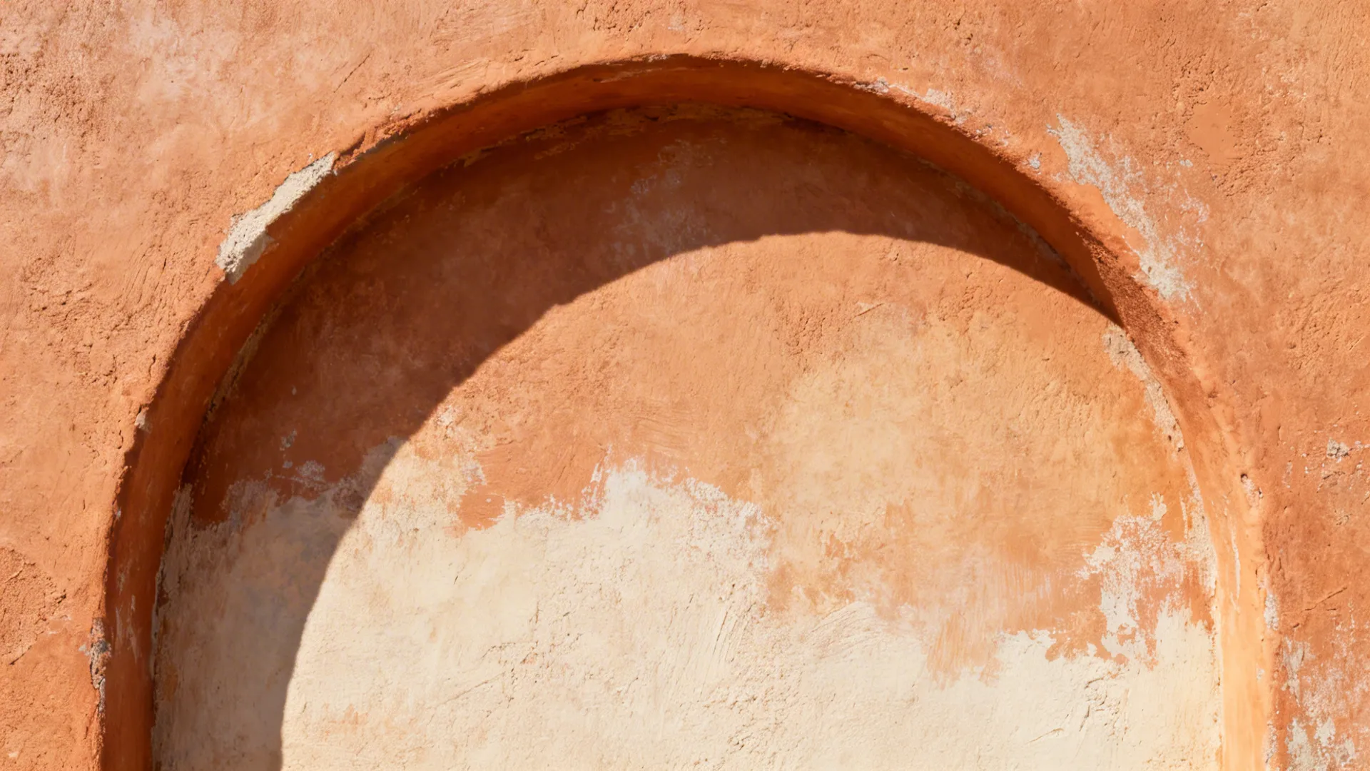 Close up of an orange textured wall featuring a curved niche and shadows from the sun