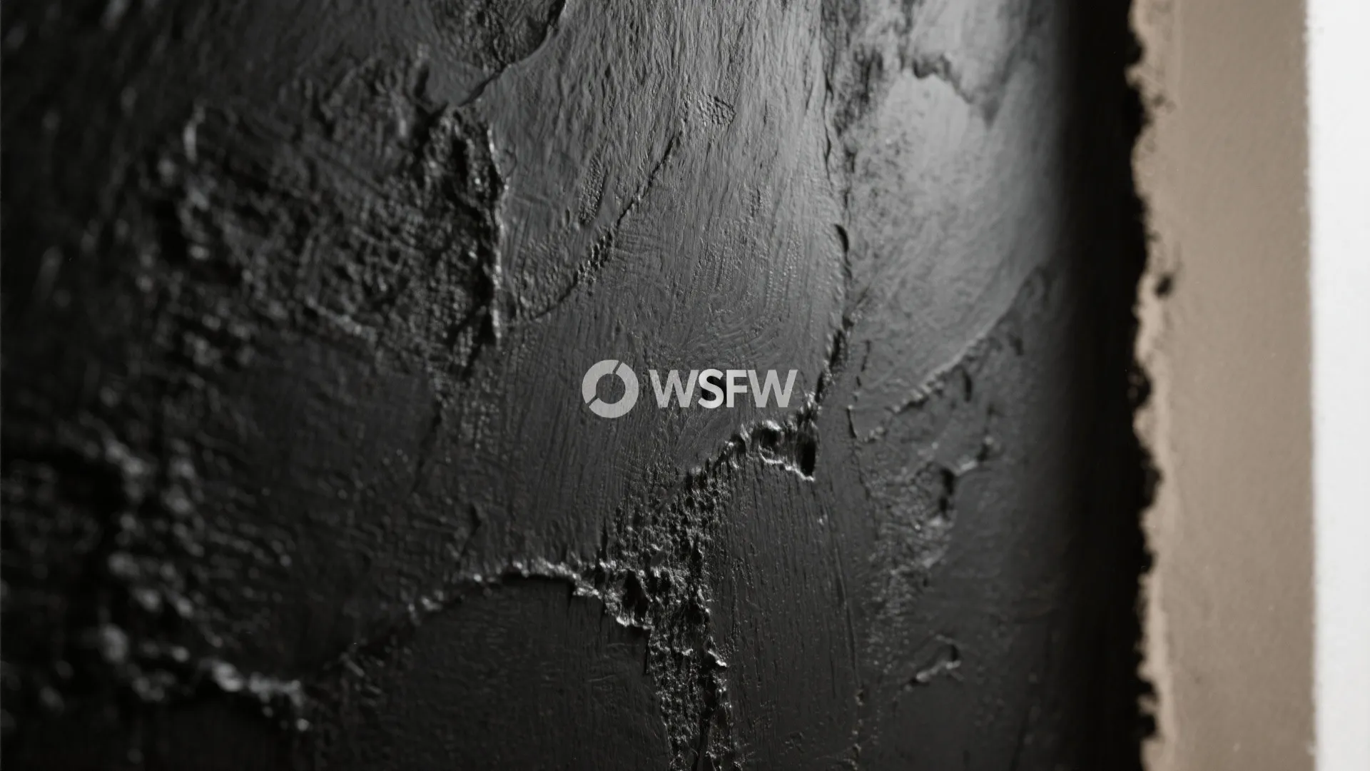 Close up view of a textured black wall with rough paint finish and a white logo