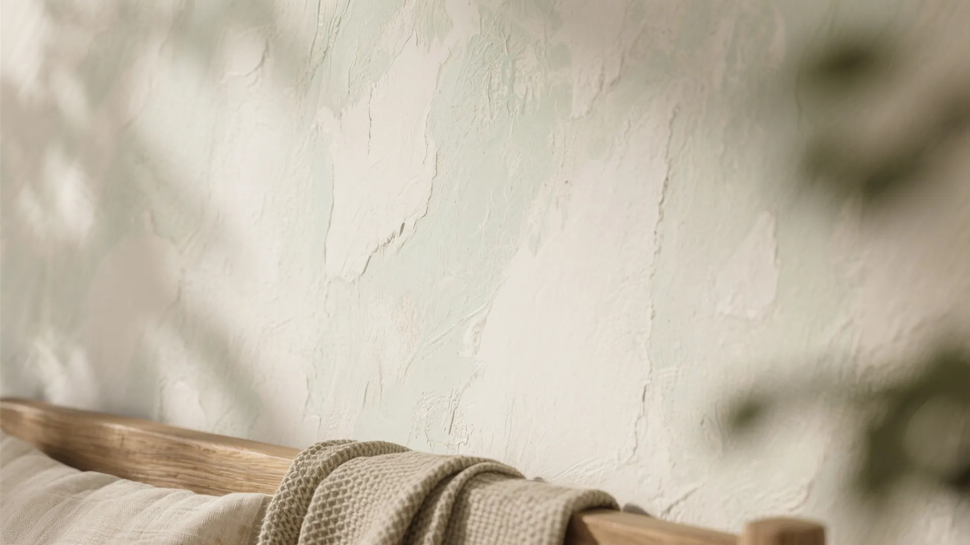Close up view of textured white wall surface with soft shadows and wooden furniture edge