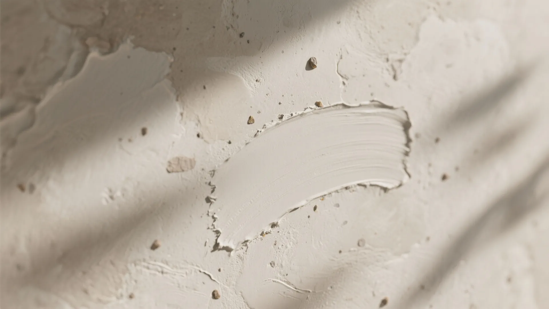 Close up of beige textured wall plaster with smooth brush strokes and small stones in sunlight
