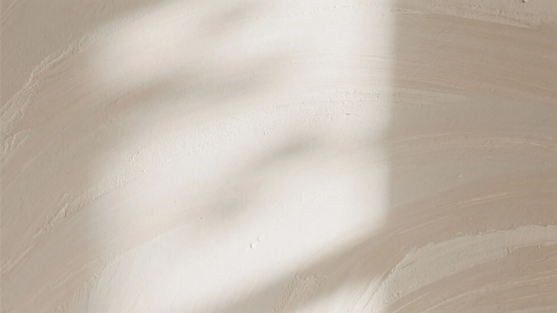 Detailed view of beige textured wall surface with soft brush marks and subtle natural lighting