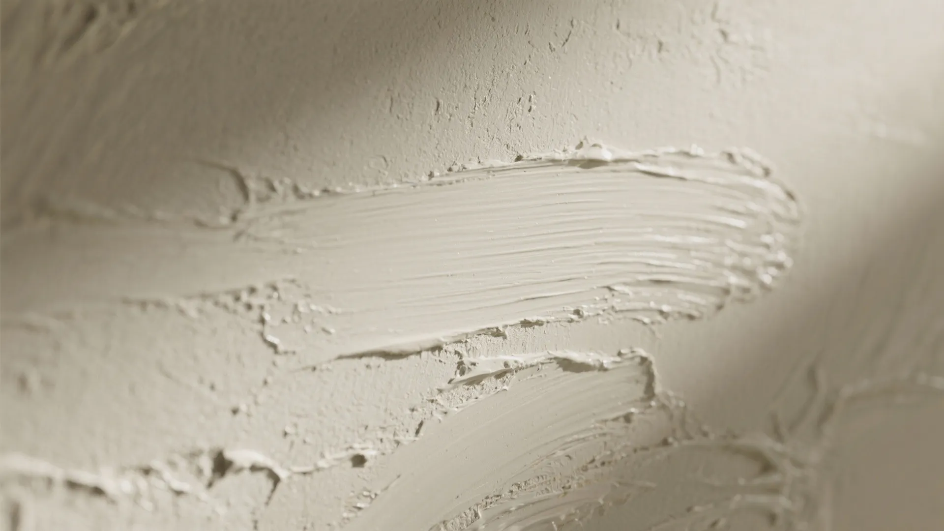 Close up view of a textured wall with beige paint showing brush strokes and natural light