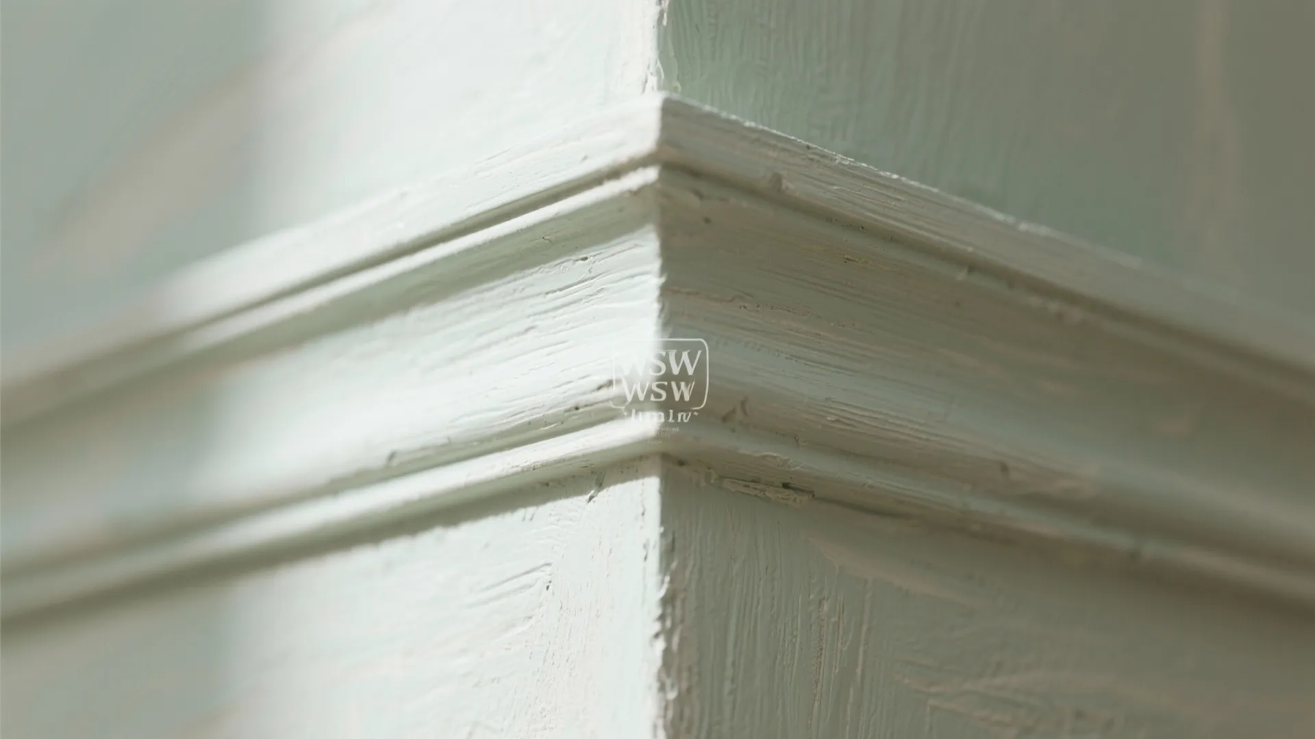 Detail of a light green painted wall corner featuring decorative wall panel molding and texture