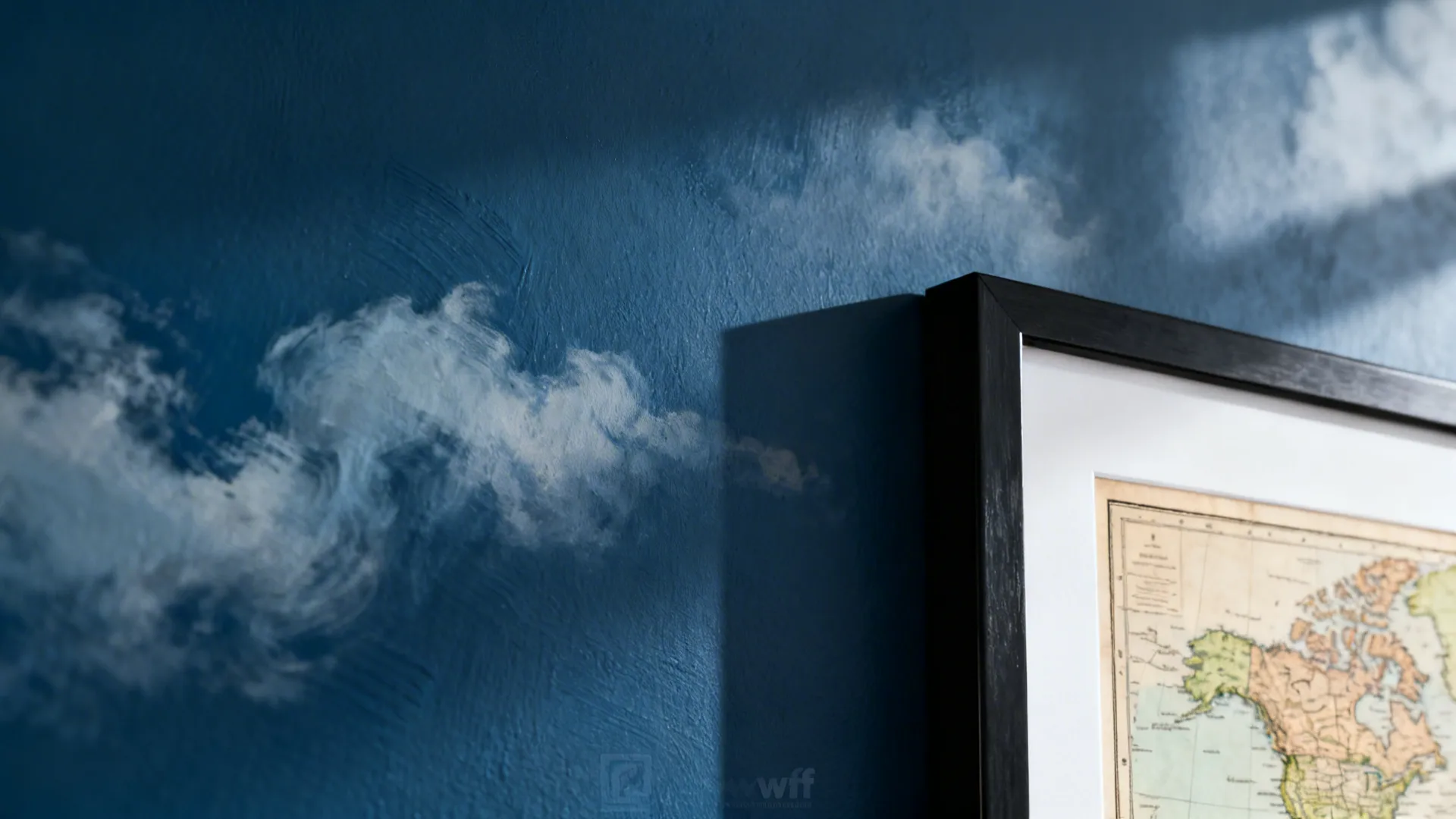 Close up of blue wall with painted white clouds and a black framed world map
