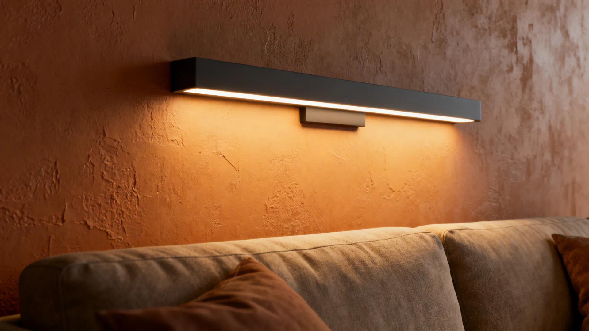 Slim linear LED sconce above a sofa casting warm, even light on a textured plaster wall.