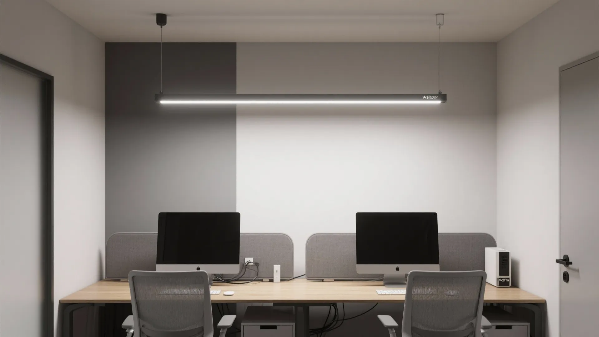 Modern office workspace featuring a long black ceiling light above a wooden desk with computers