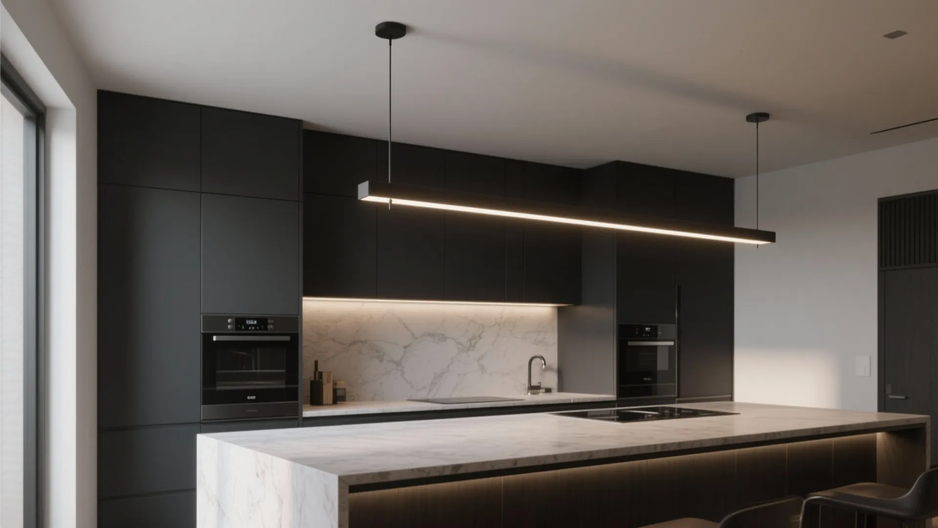 Contemporary black kitchen cabinets with a long linear ceiling light hanging over a white marble island