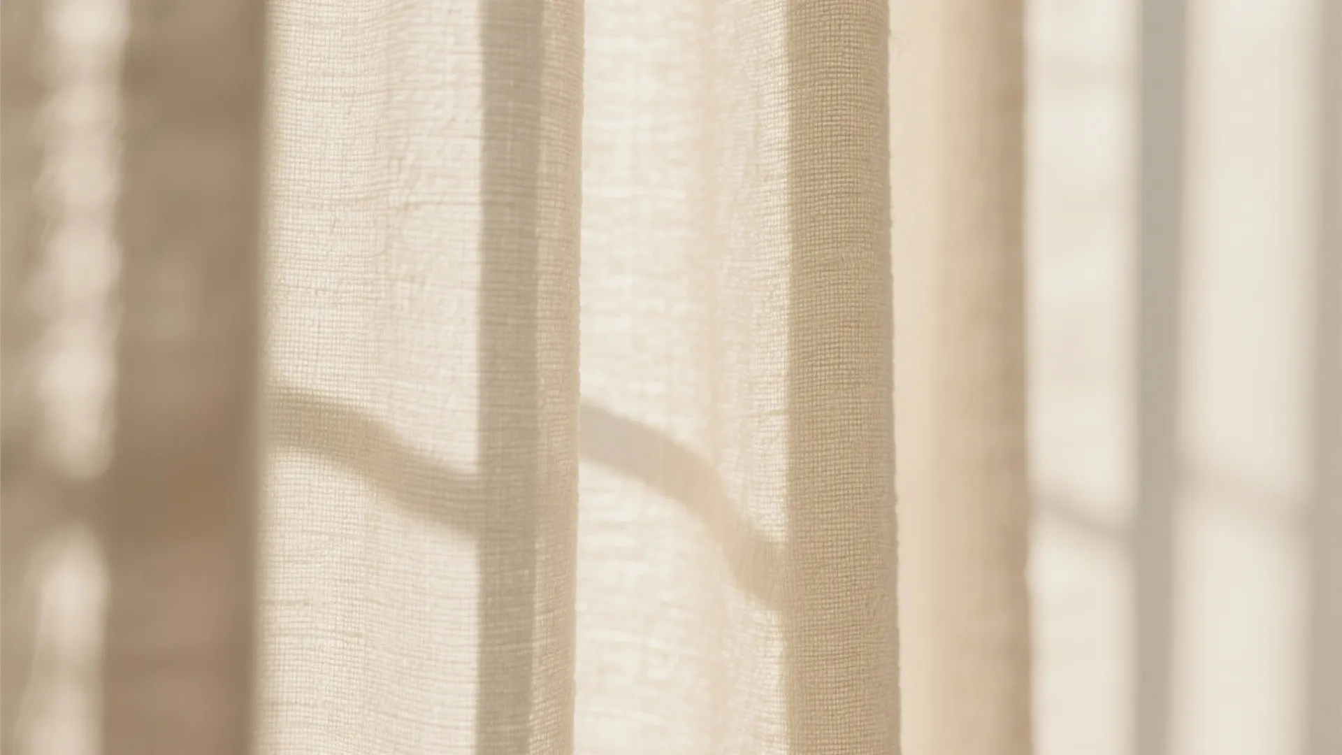Close-up of beige linen curtain fabric with soft sunlight shadows from a nearby window frame