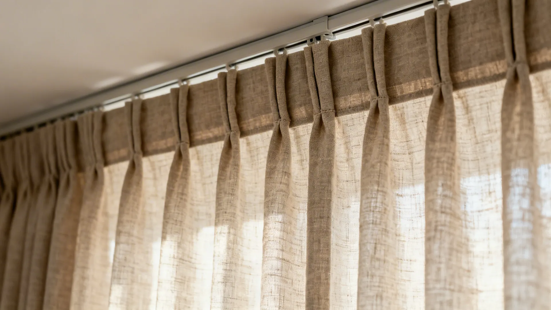 Close-up of linen drapery pinch-pleat and ceiling track with a precise floor-kiss hem.