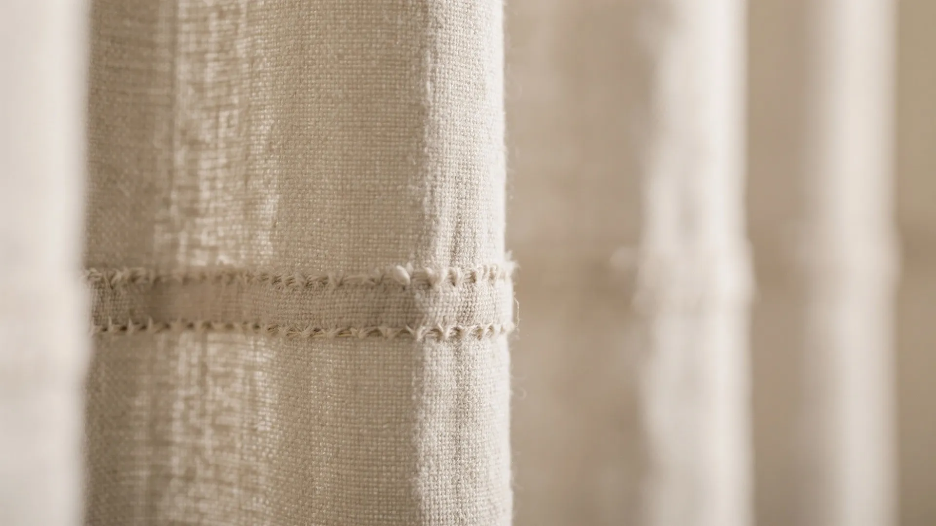 Macro of linen-blend curtain fabric with slub texture and detailed stitching under soft daylight.