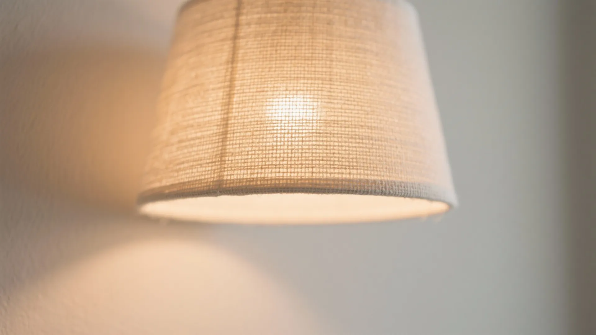 Close up view of a fabric lampshade with warm glowing light on a simple wall