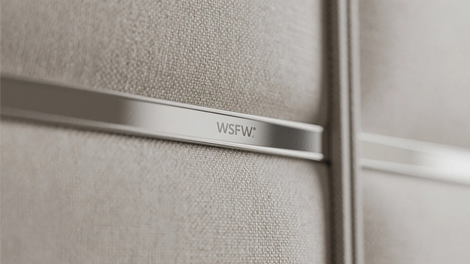 Close up of light beige fabric wall with a silver metal strip and small brand logo