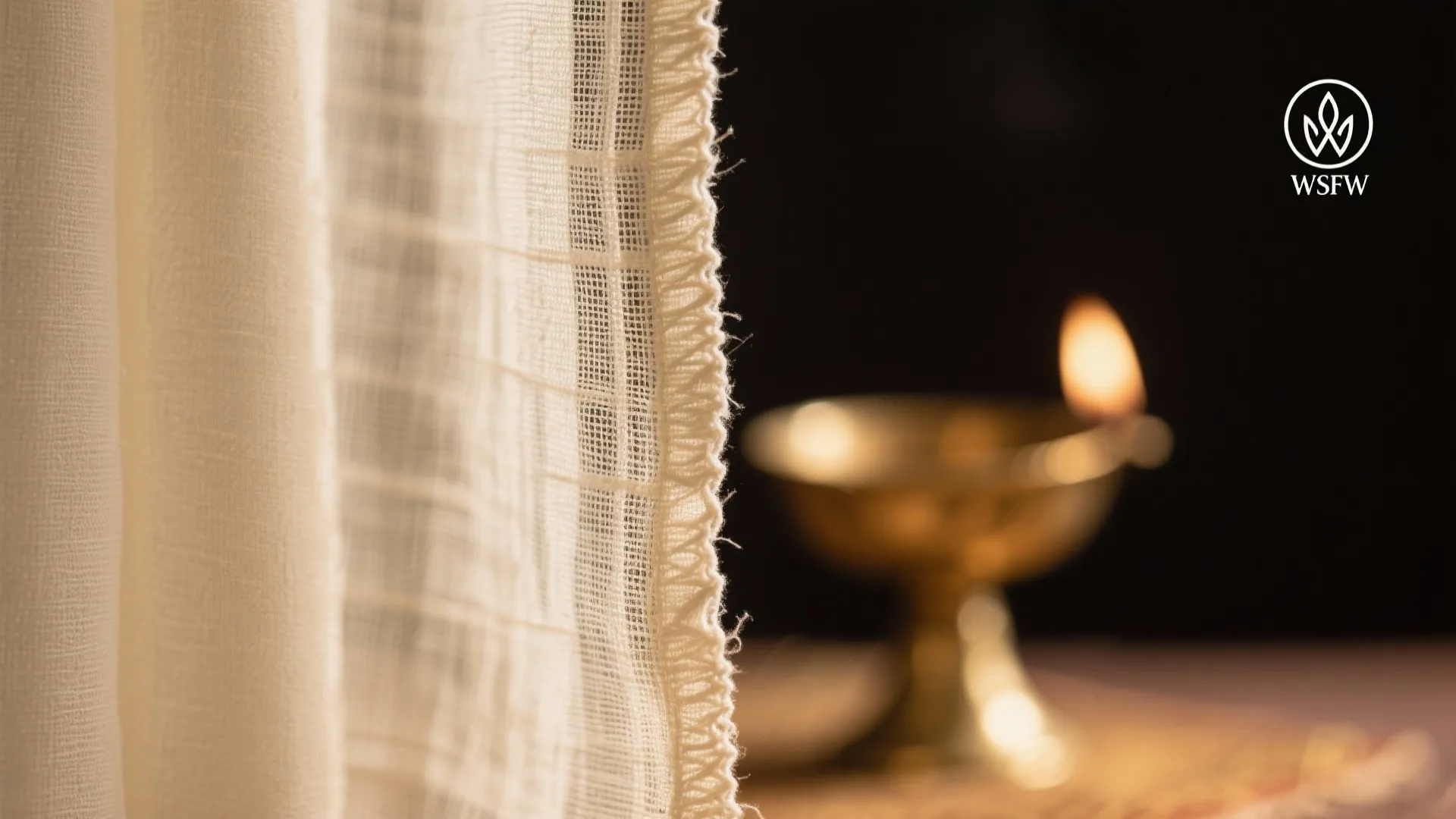 Close up of cream curtain edge with a small metal oil lamp glowing in background
