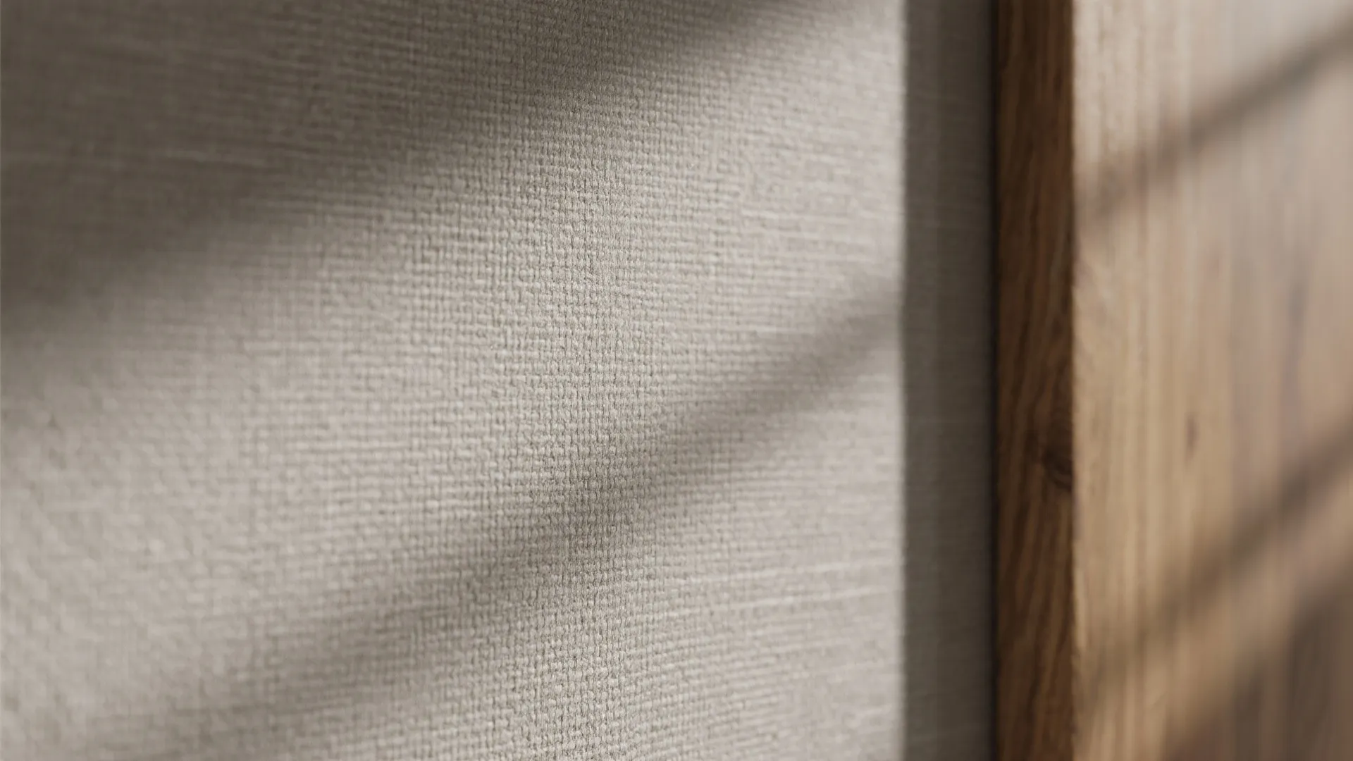 Close up view of beige wall fabric texture with soft shadows and wooden frame detail