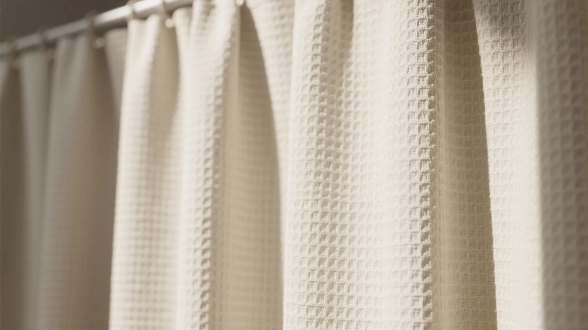 Close up view of cream white textured grid curtain hanging on a silver metal rod