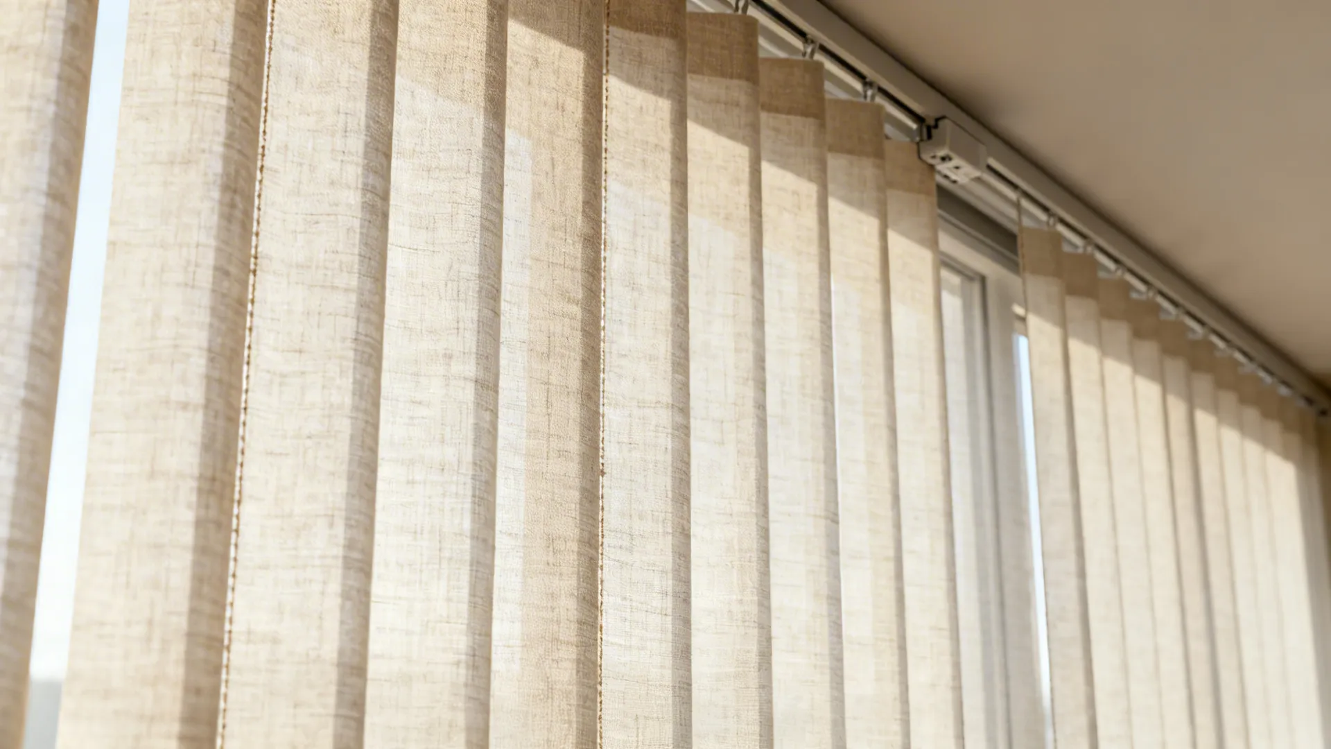 Close-up of linen-texture vertical blinds filtering daylight in a wide window.