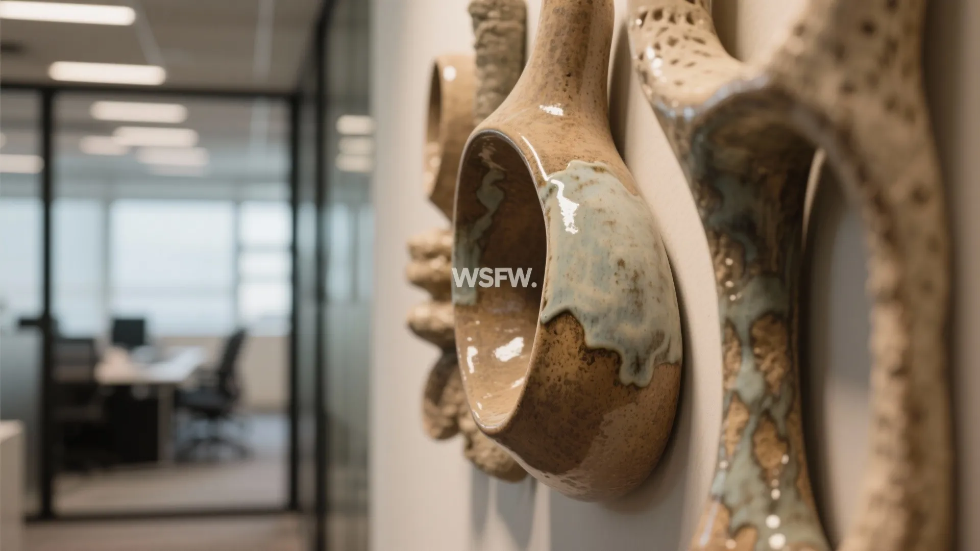 Close up of handmade ceramic wall art hanging in a modern office with glass door background