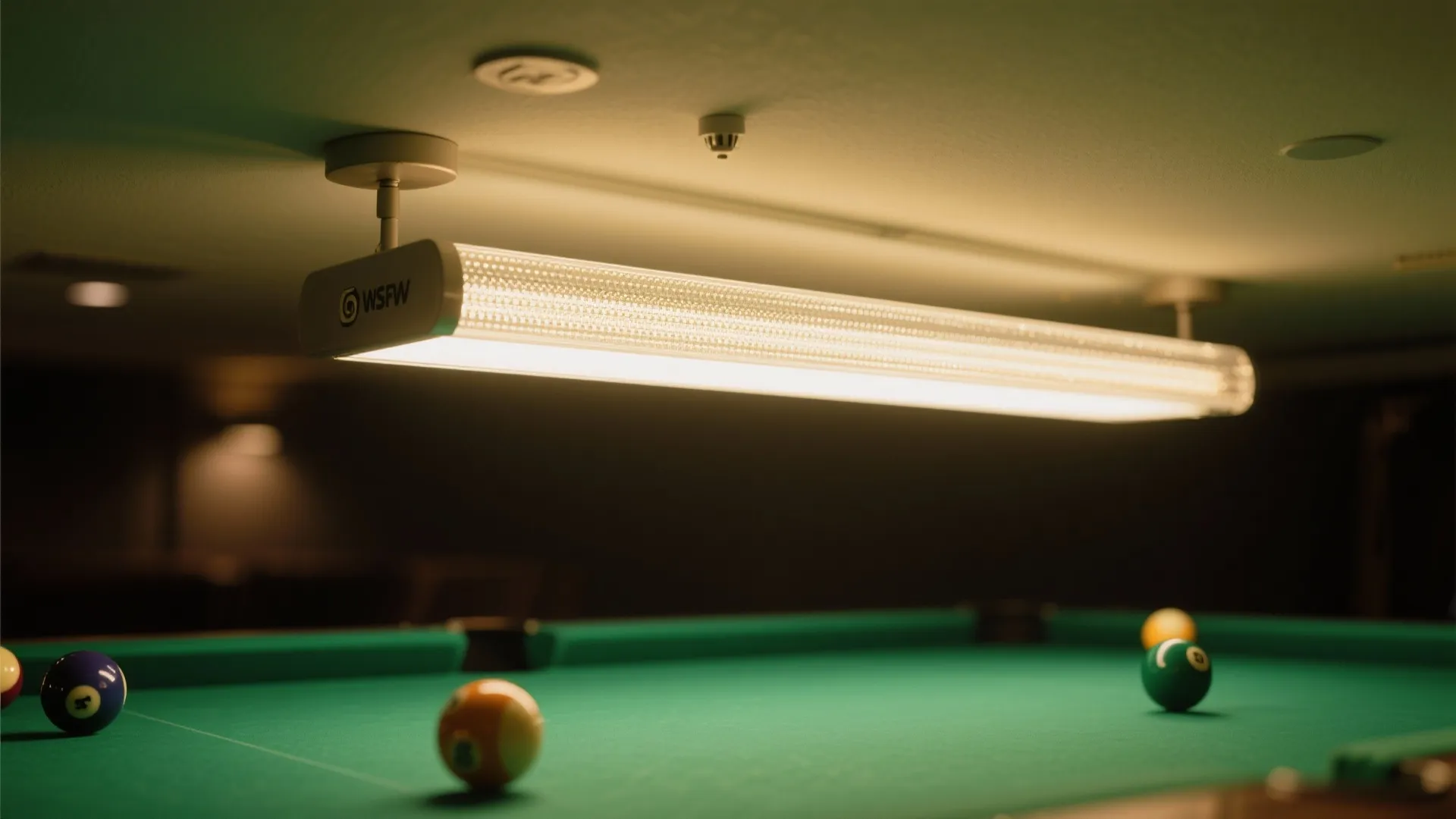 Long modern ceiling light hanging over a green pool table with colorful balls and cue