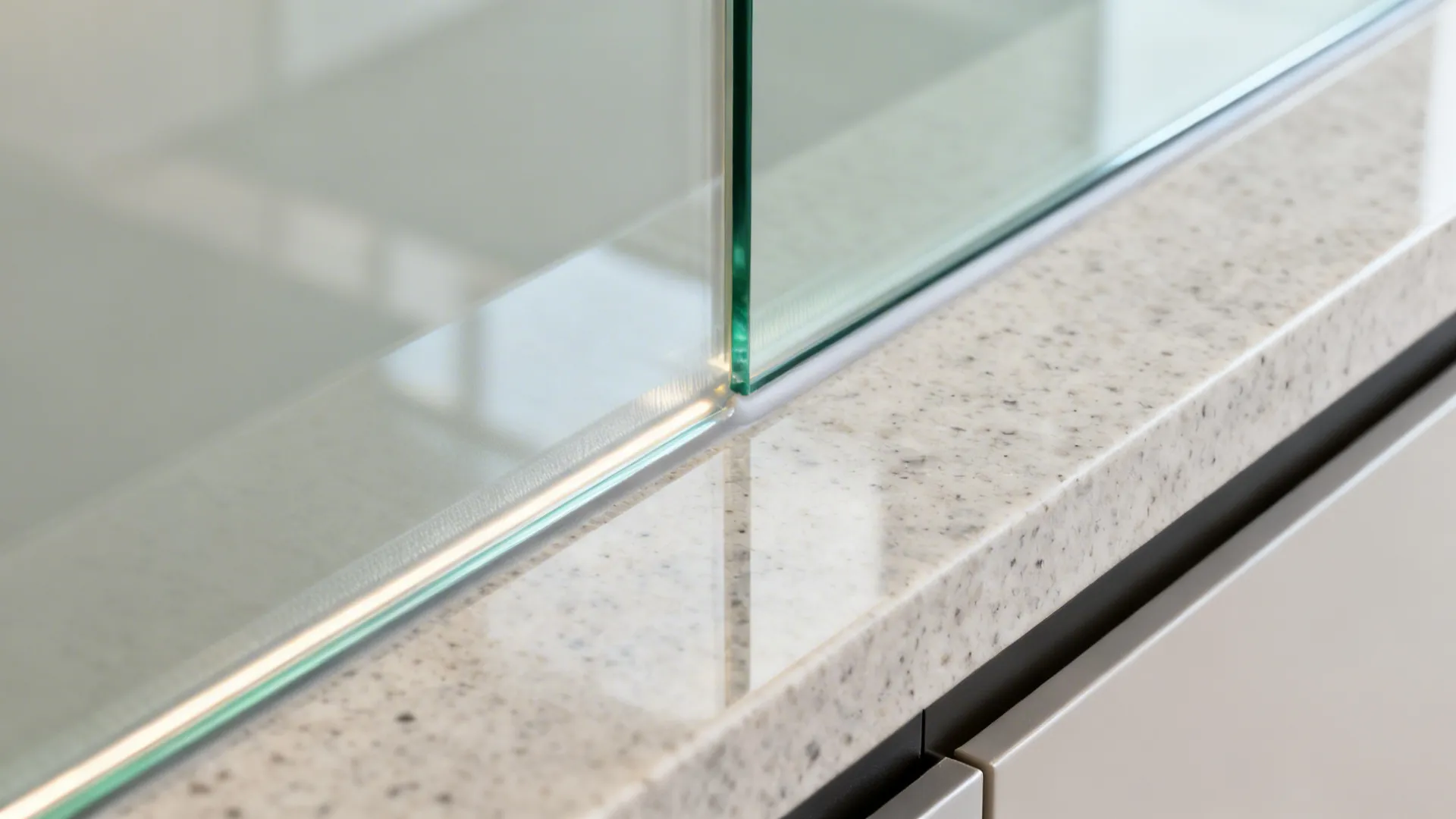 Close up of a clear glass wall panel meeting a marble countertop with bright light