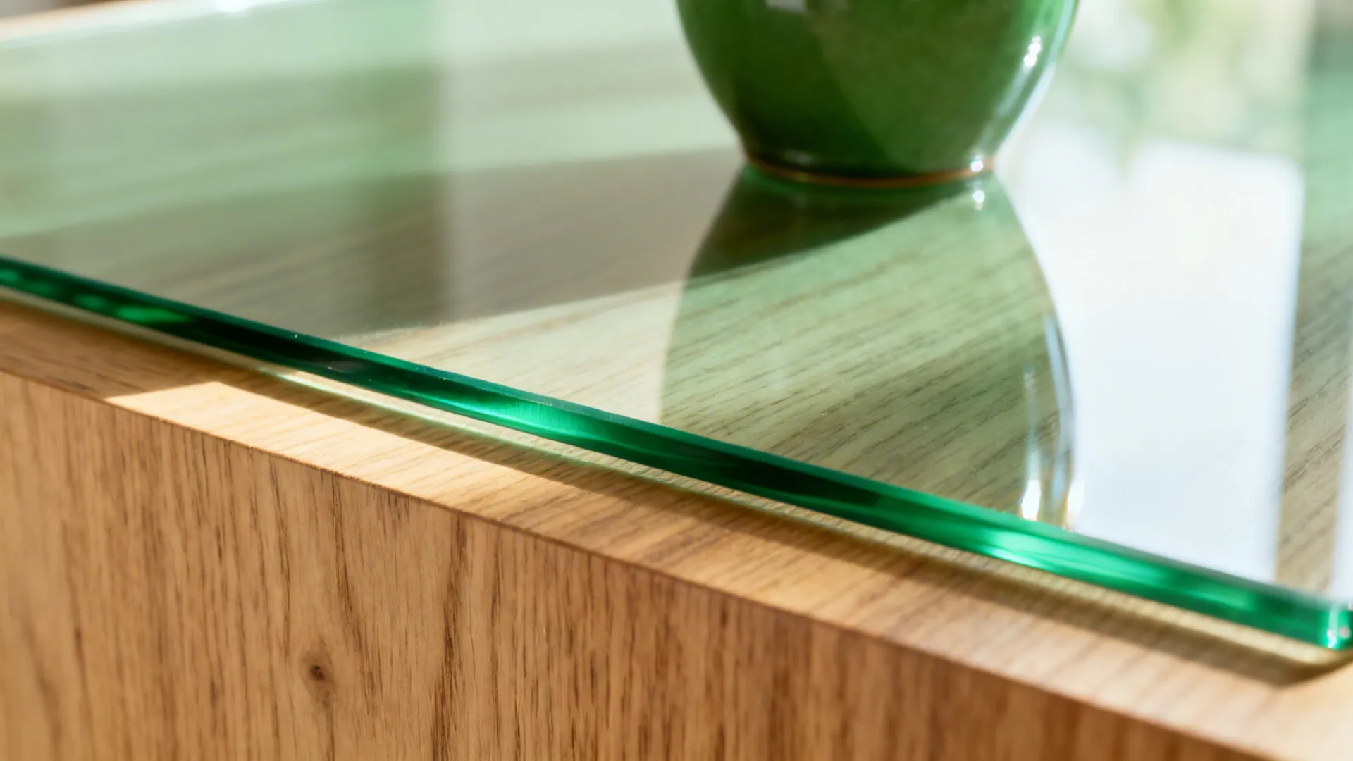 Close up of glass table top edge on wooden furniture with reflection of green bowl