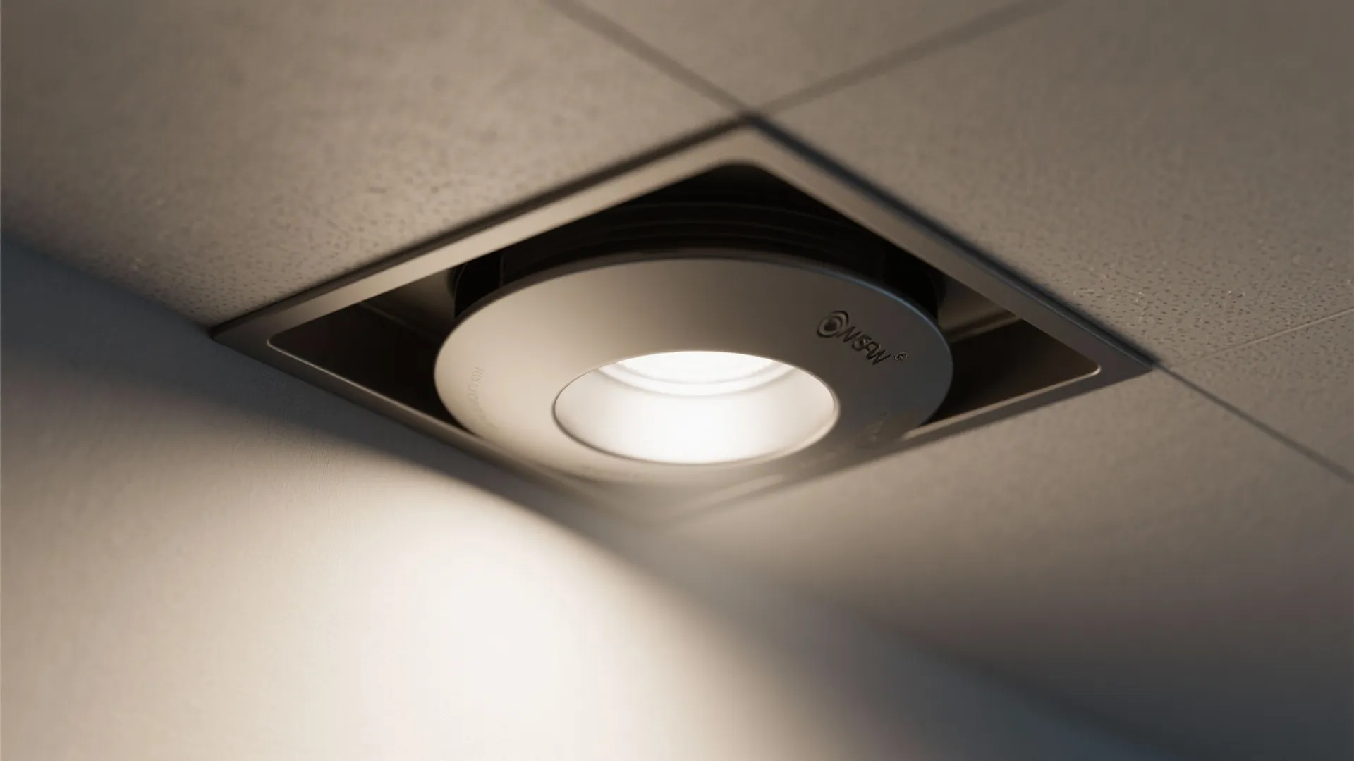 Square recessed ceiling light glowing with bright white light on a white textured office ceiling