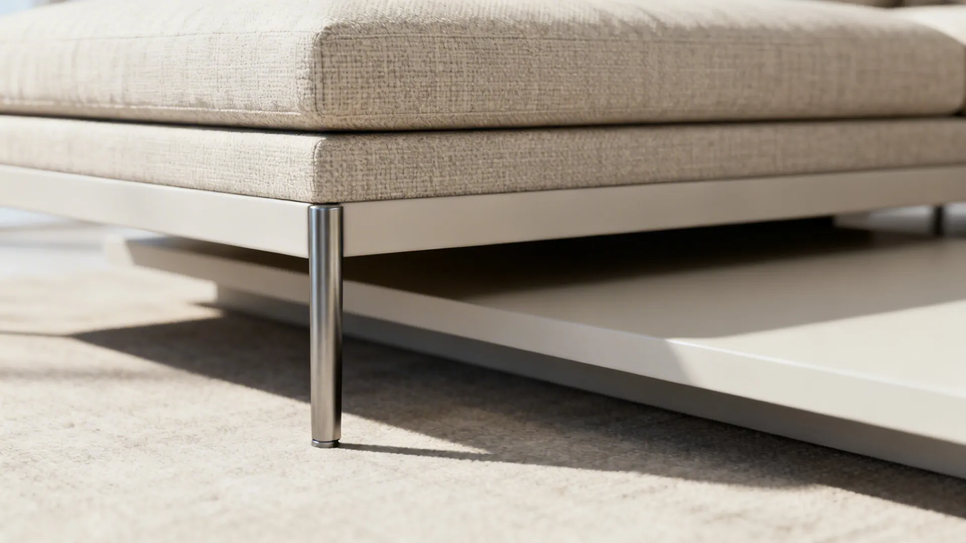 Close up view of thin metal leg supporting a beige fabric sofa on a light carpet