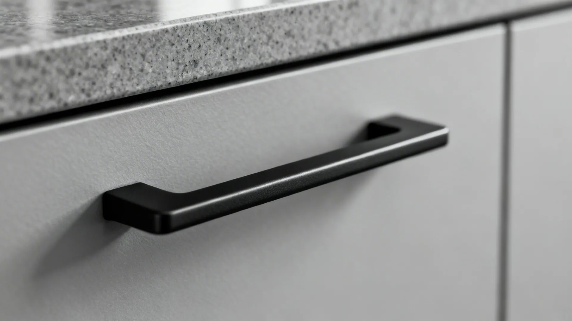 Macro of a matte black handle on a soft grey cabinet front in natural light.