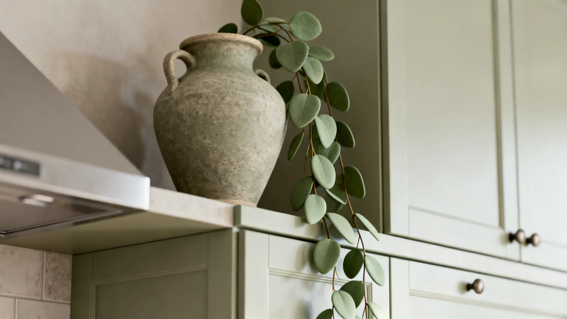 Macro view of matte ceramic texture and faux plant leaves above kitchen cabinets.