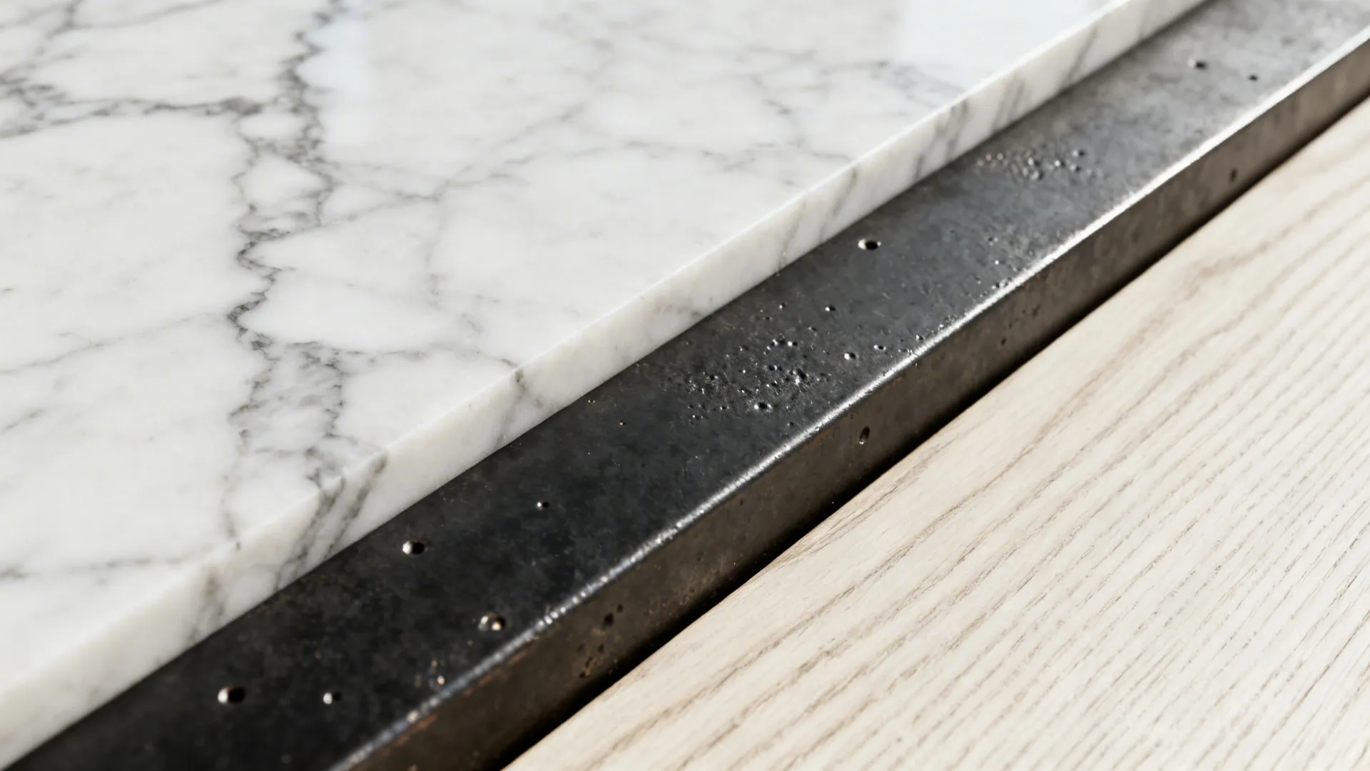 Macro view of honed marble veining, white oak grain, and textured blackened steel.