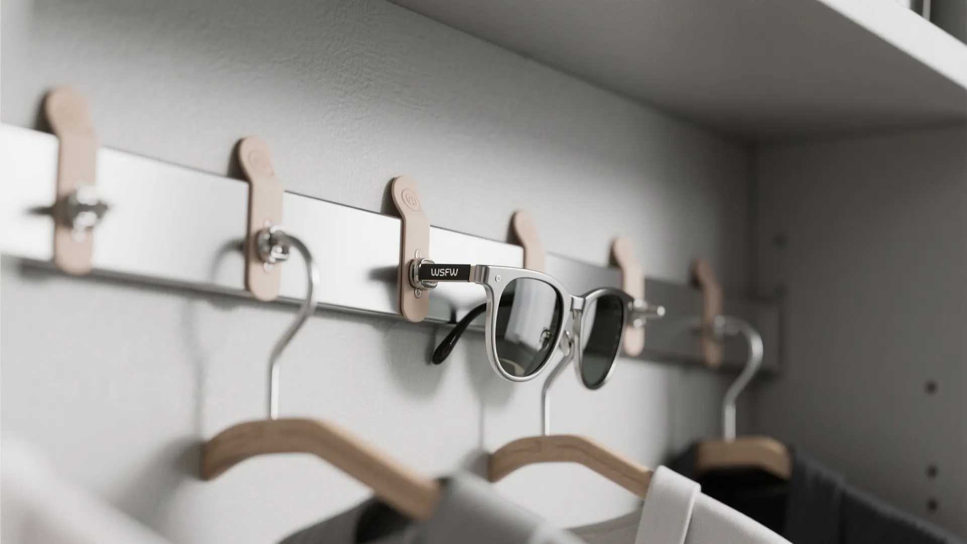 Silver metal magnetic strip on a white wall holding one pair of sunglasses and clothes hangers