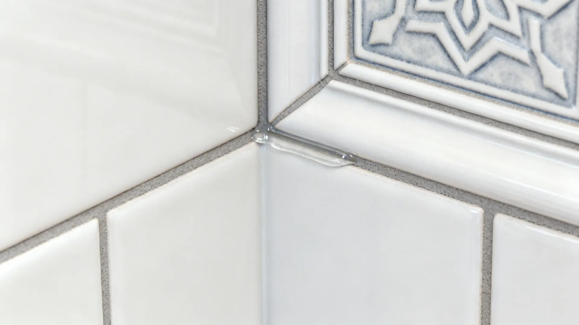 Close up shot showing clear liquid sealant applied to a corner joint of white tiles