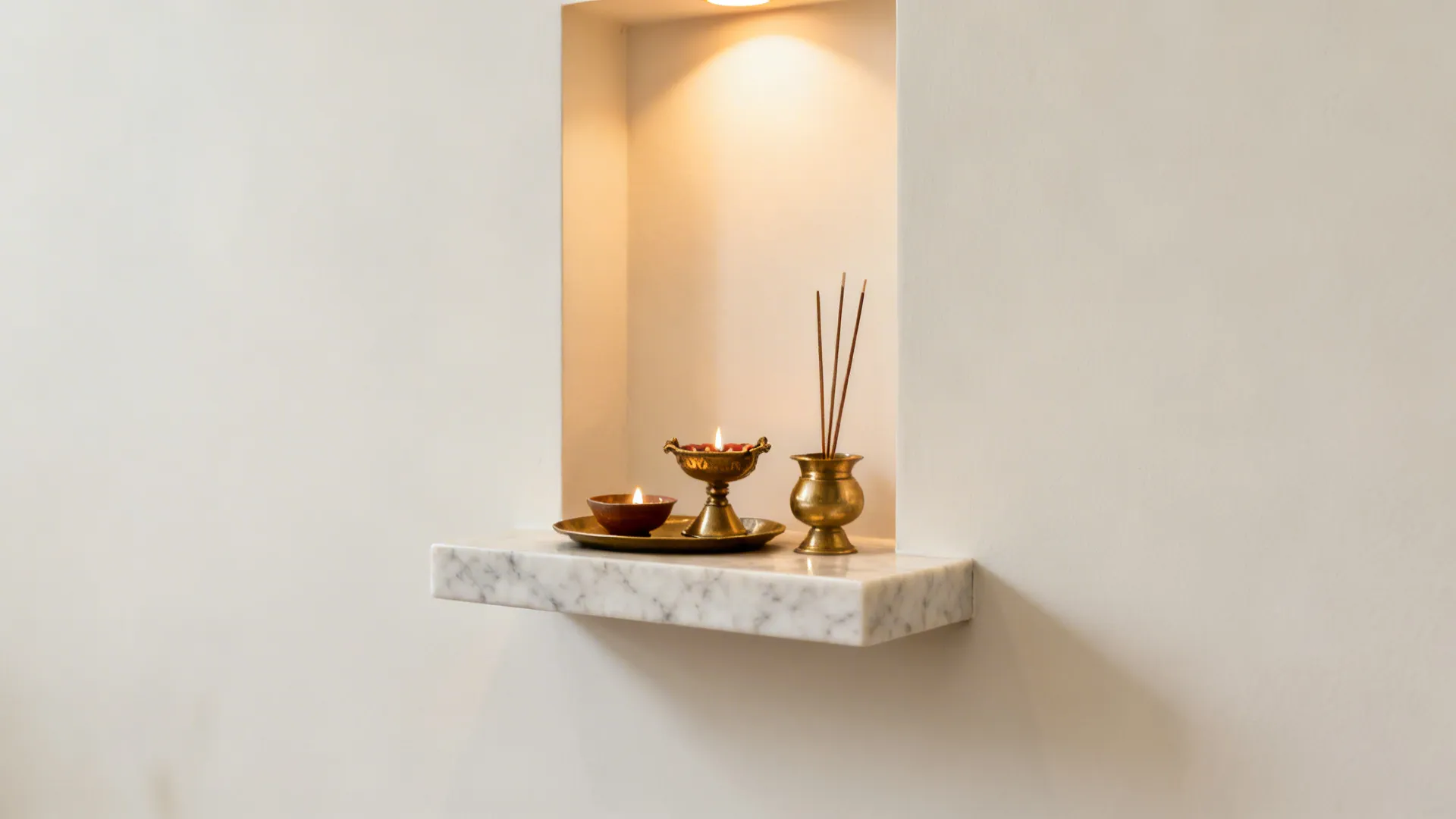 Honed marble pooja shelf with a small upstand and brass accessories on a tray under soft warm light.