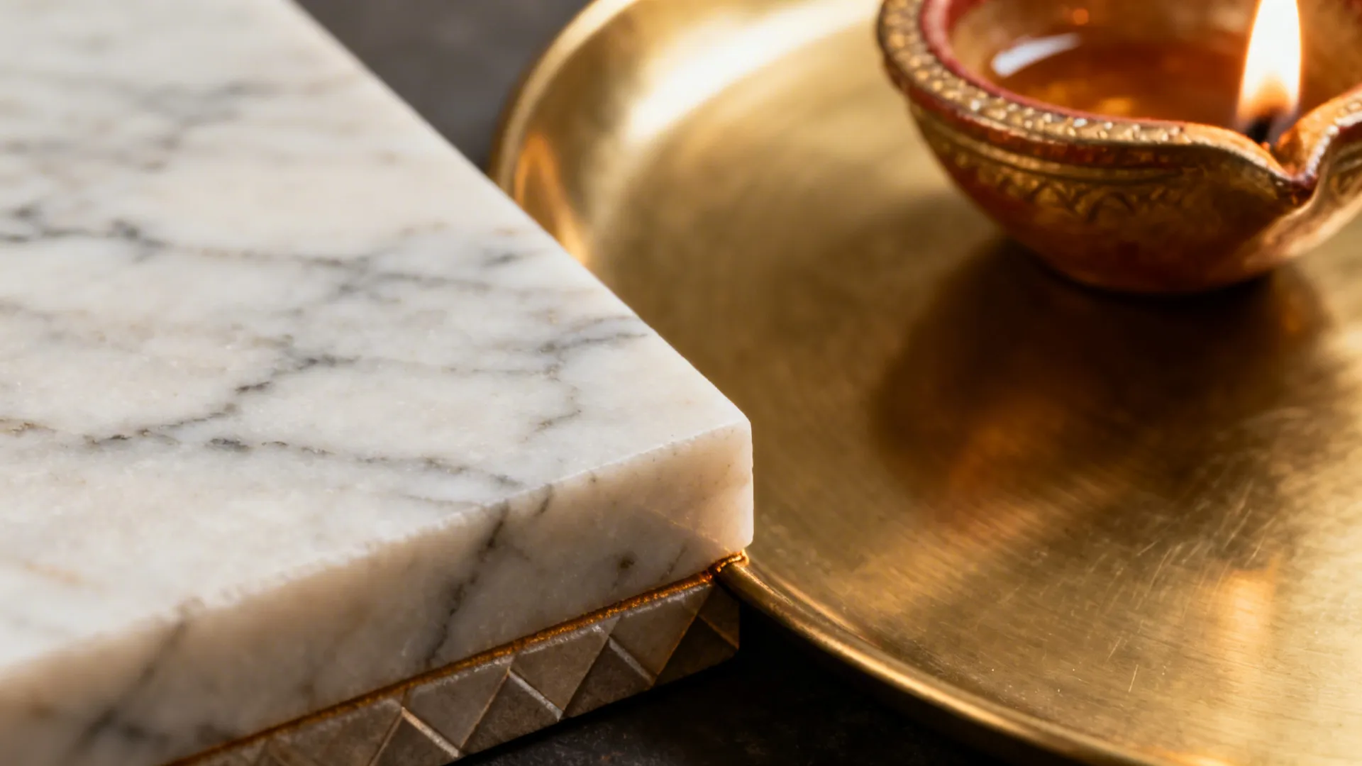 Close-up of a honed marble altar edge meeting a brushed brass tray with a diya in warm light.