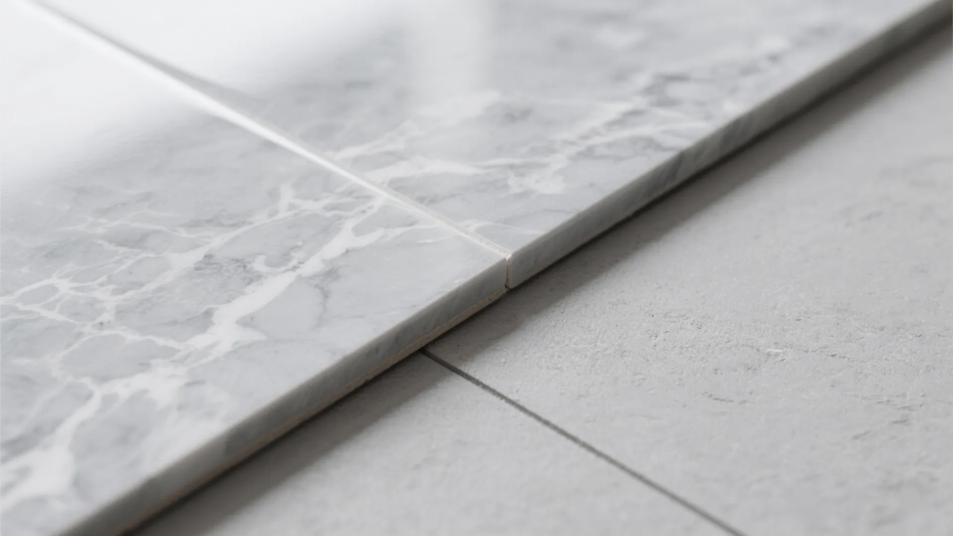 Close up of a polished white marble tile meeting a textured grey stone floor tile