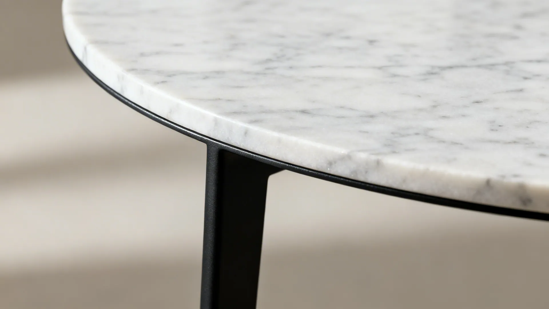 Macro detail of a honed marble round tabletop and slim matte black steel frame.