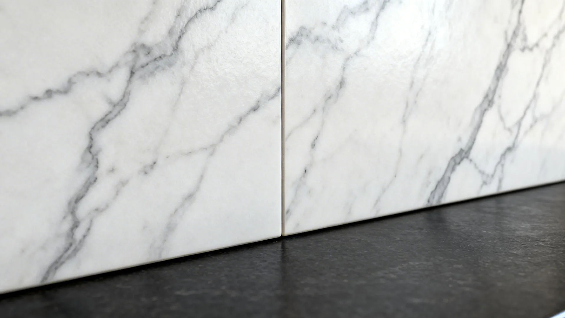 Close-up of marble-look porcelain slab backsplash with soft gray veining meeting dark countertop